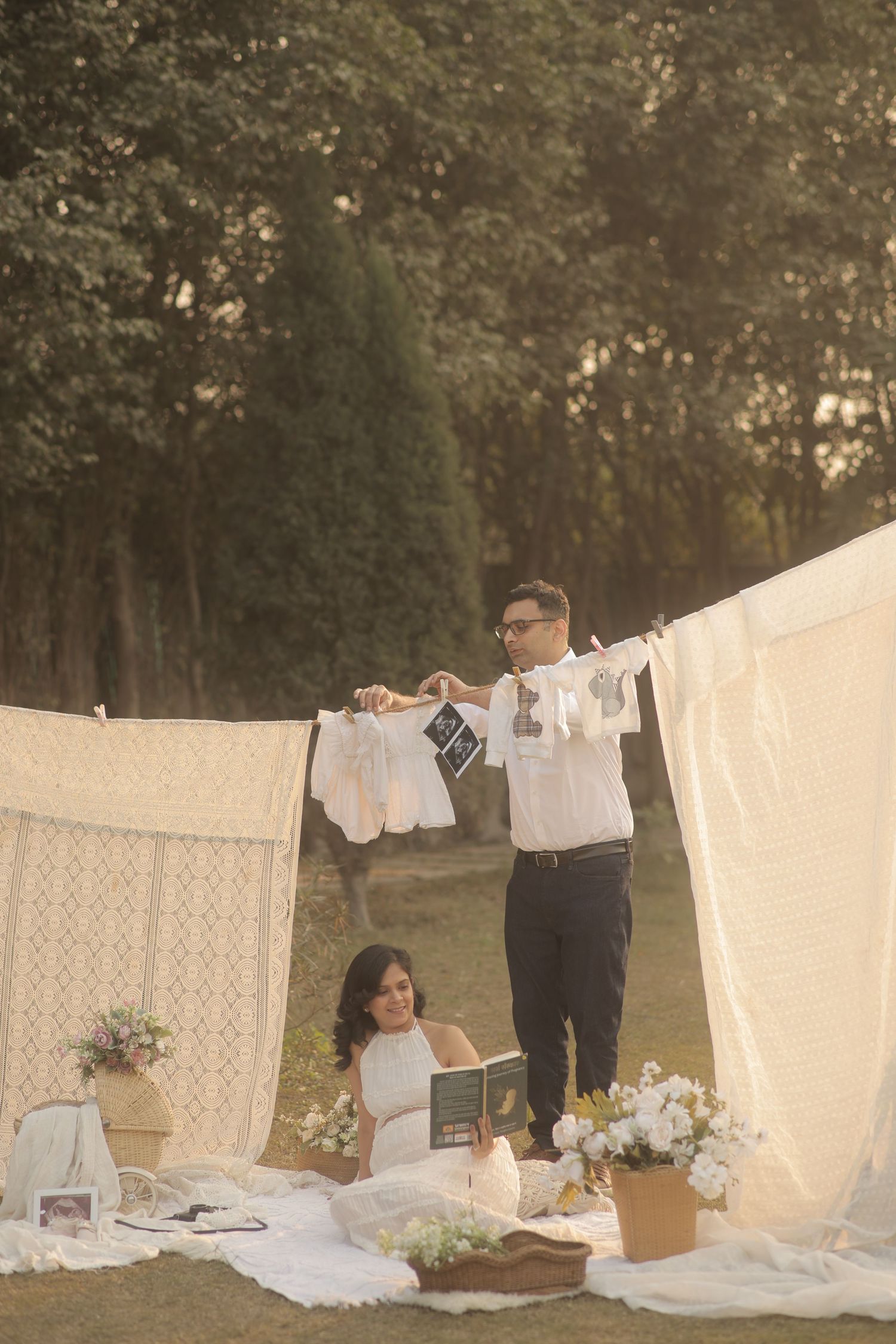 A vintage-inspired outdoor scene with white lace tablecloths and linens hanging on clotheslines among trees and flowers.