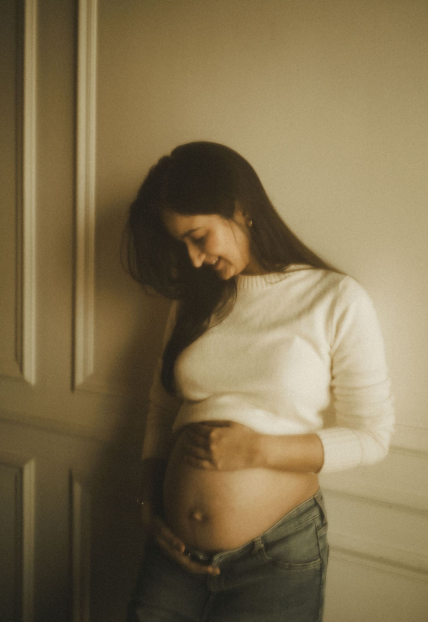 A series of four intimate photographs showing a person in a white sweater revealing their pregnant belly against a neutral wall.