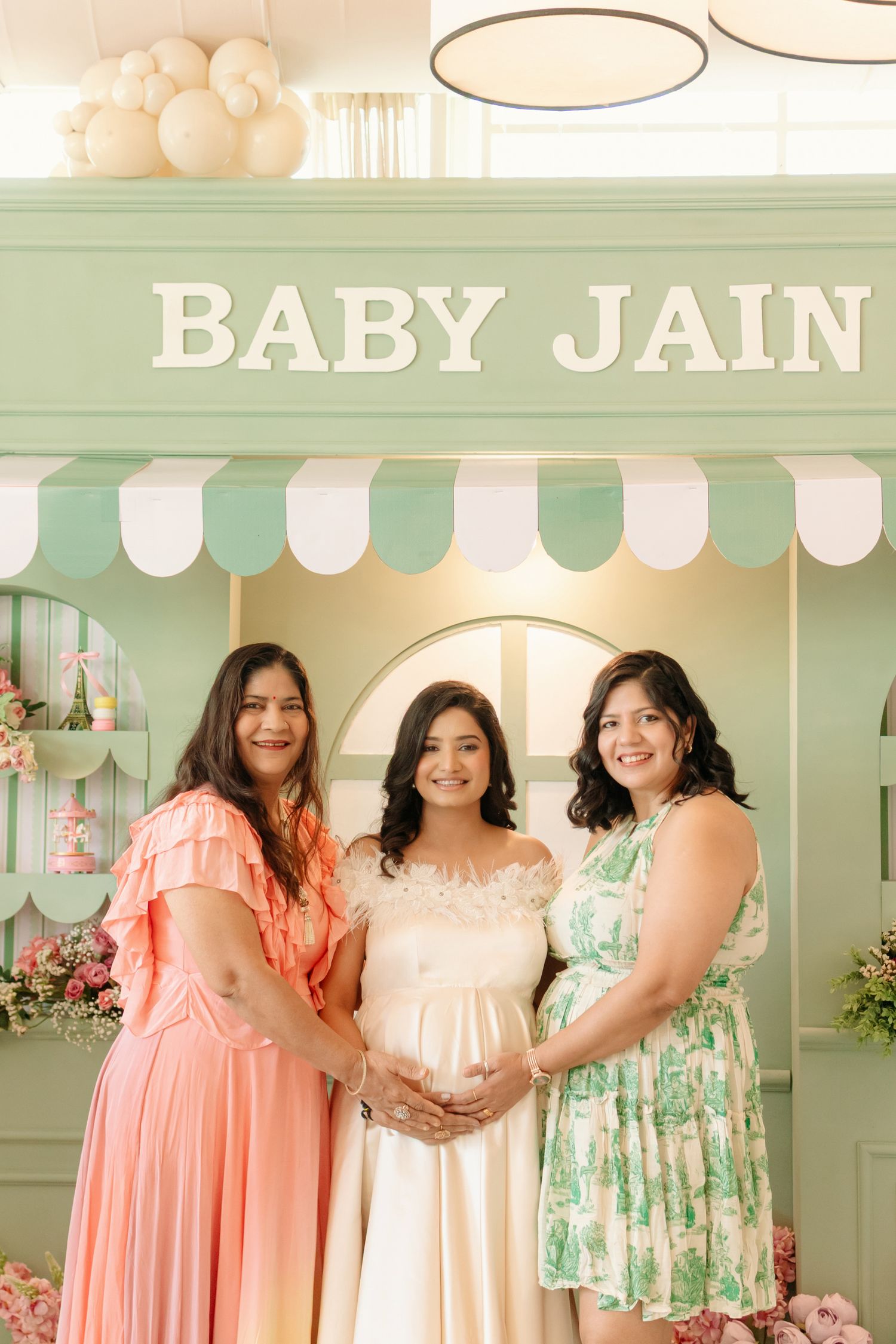 Three women pose together at a Baby Jain baby shower in front of a mint green decorative backdrop.
