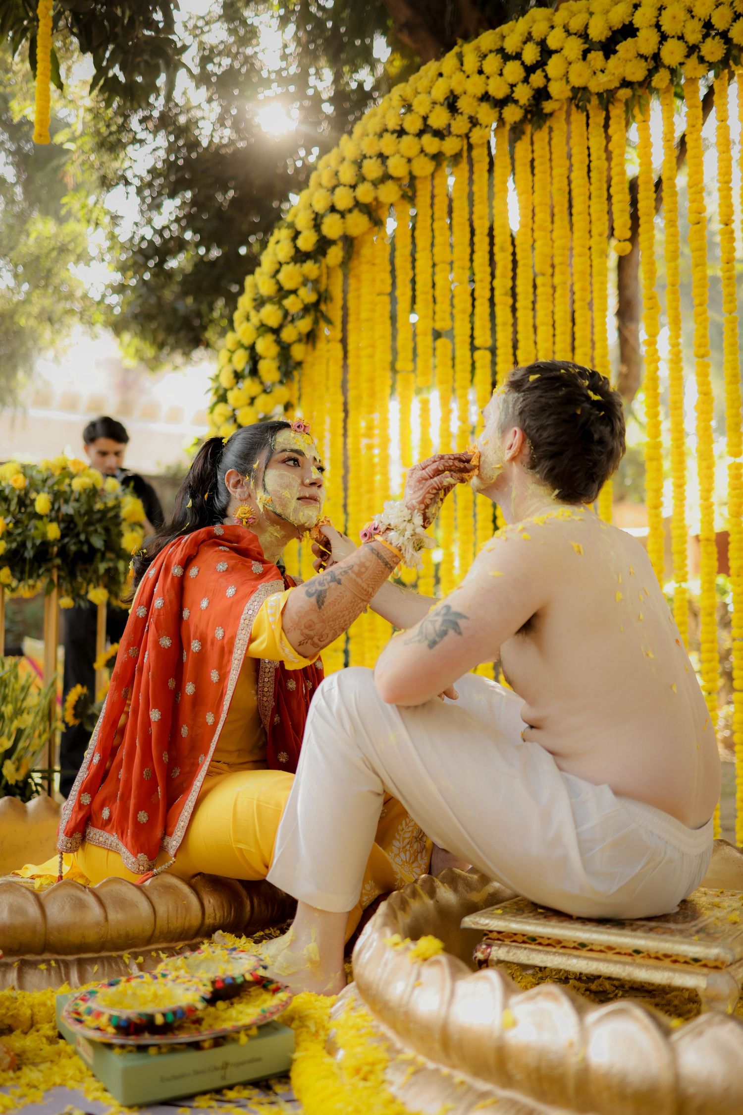 Traditional Indian haldi ceremony with bright yellow marigold decorations and sunlight filtering through the backdrop.