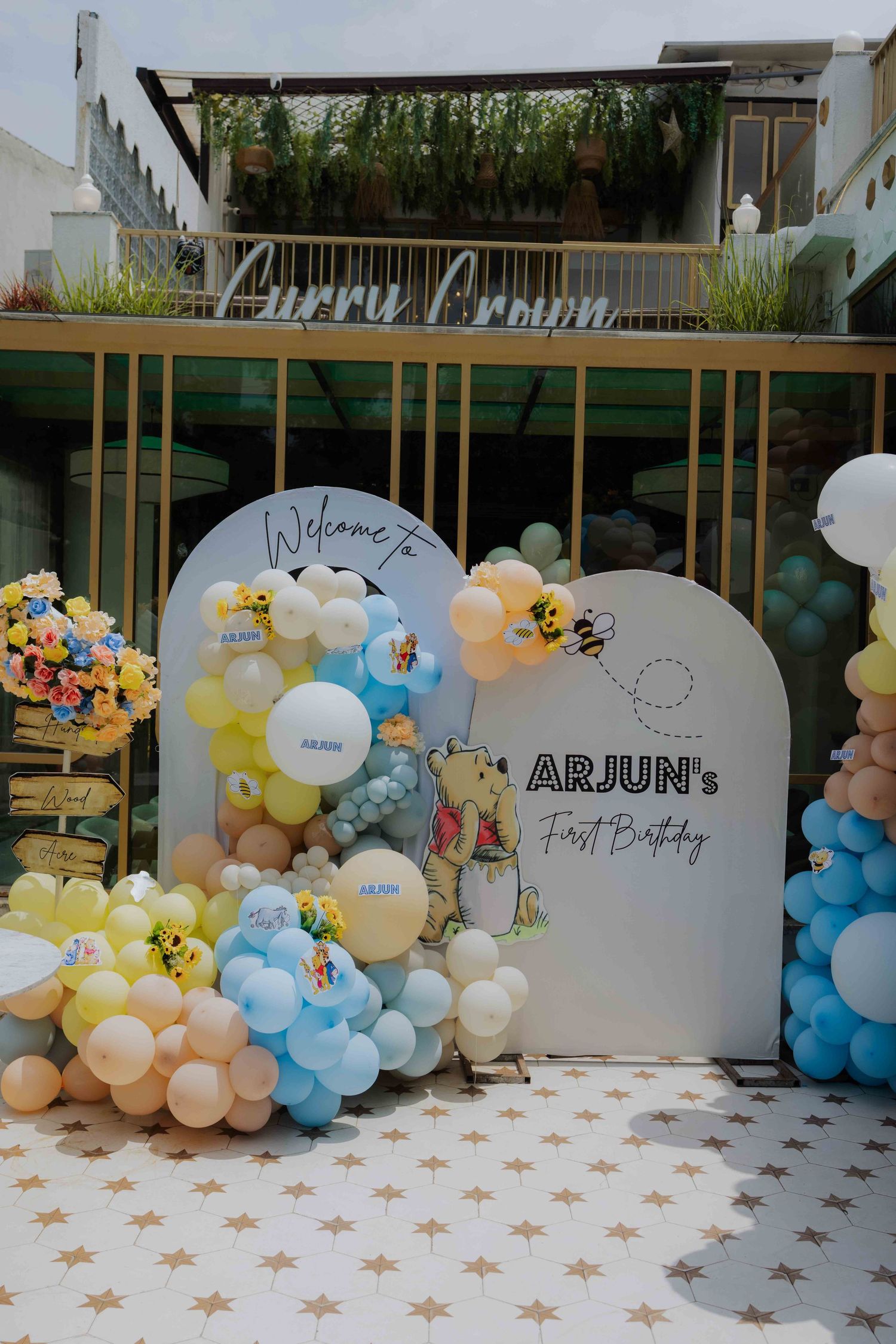 Arjun's first birthday party backdrop with colorful balloon garland in blue, yellow, and white with Winnie the Pooh theme.