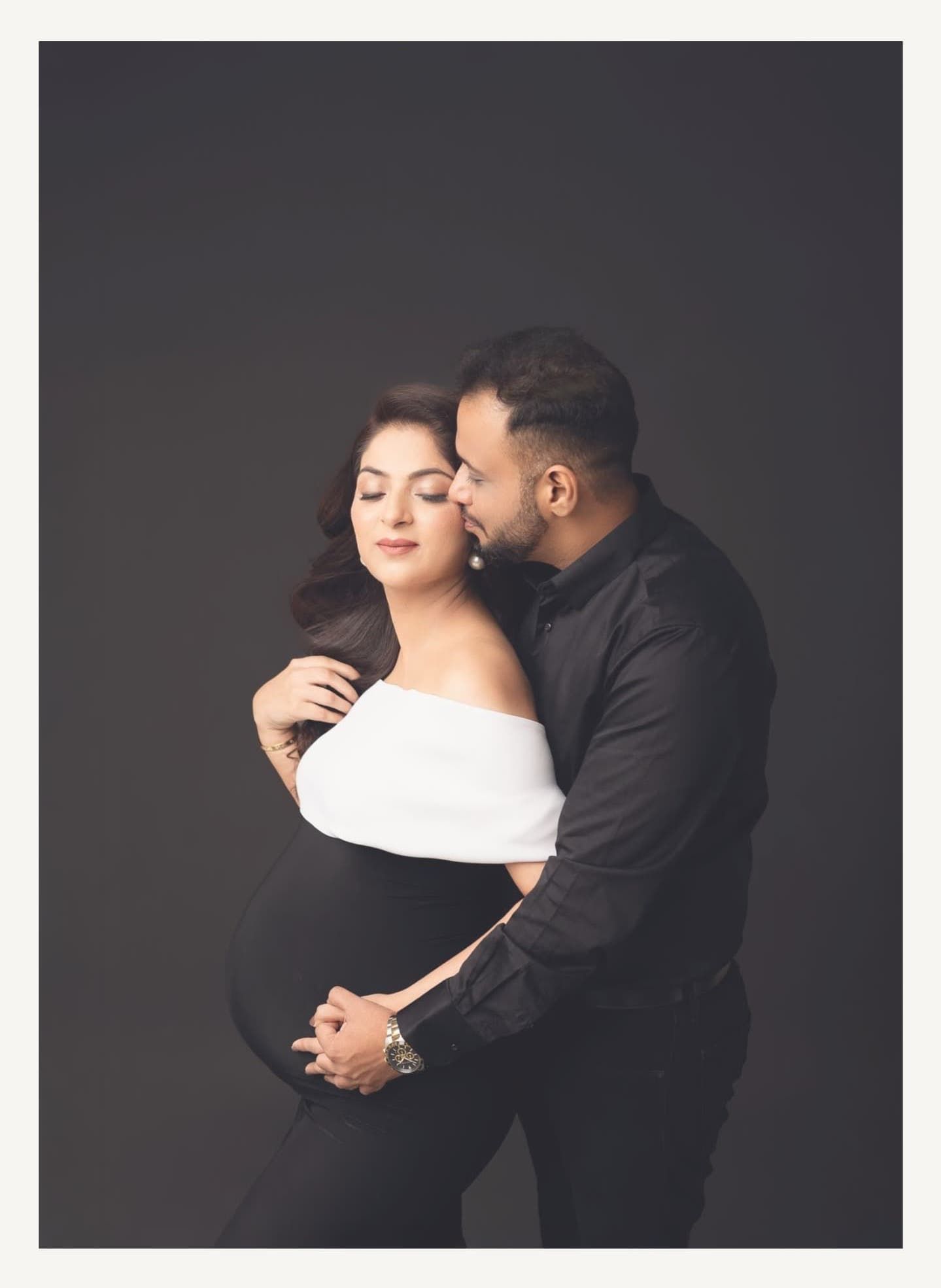 Intimate maternity portrait of expecting couple in black and white against dark background.