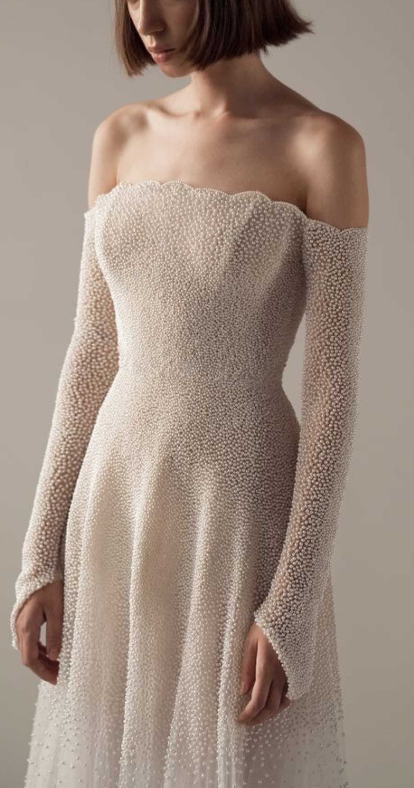 Close-up detail of beaded off-shoulder wedding gown with long sleeves and fitted silhouette.