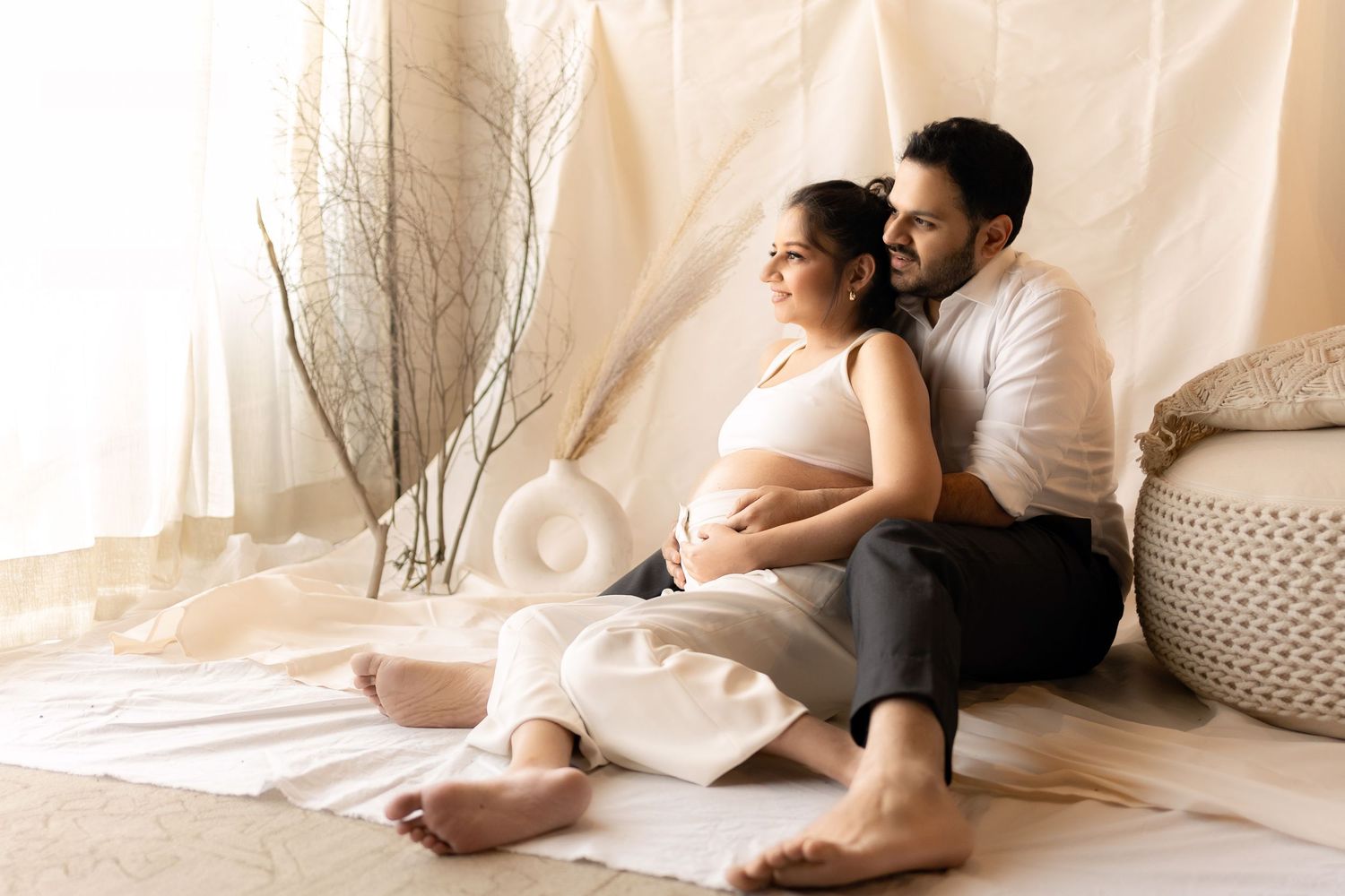 Intimate maternity photoshoot on white backdrop with couple in casual wear.