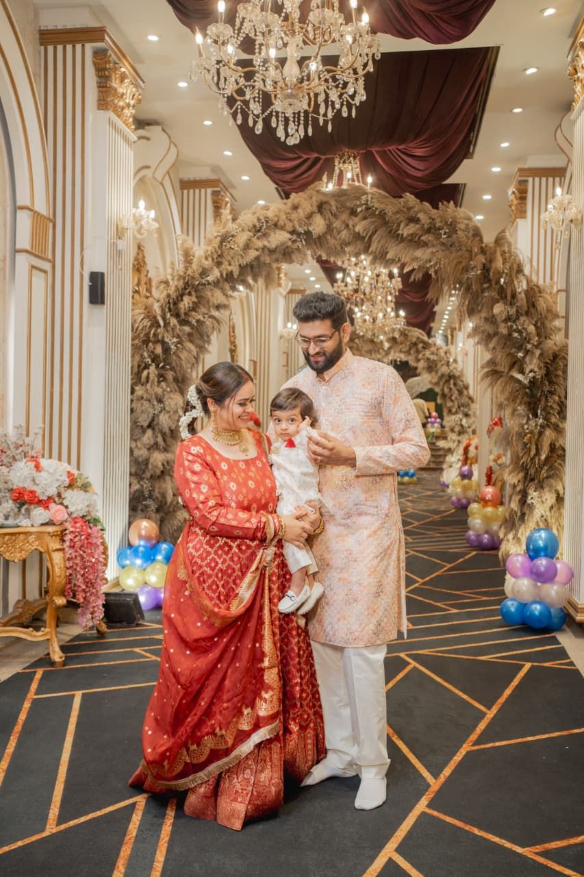 A family in traditional South Asian attire poses at an elegant decorated event hall with floral arch and chandeliers.