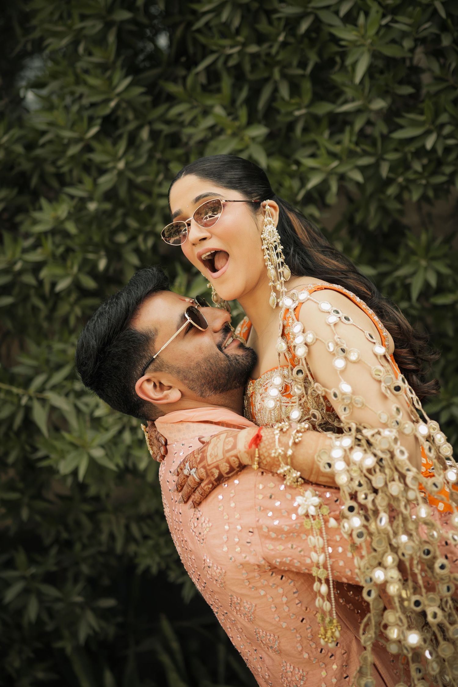 A couple in traditional attire shares romantic moments in a series of photos against a green foliage backdrop.
