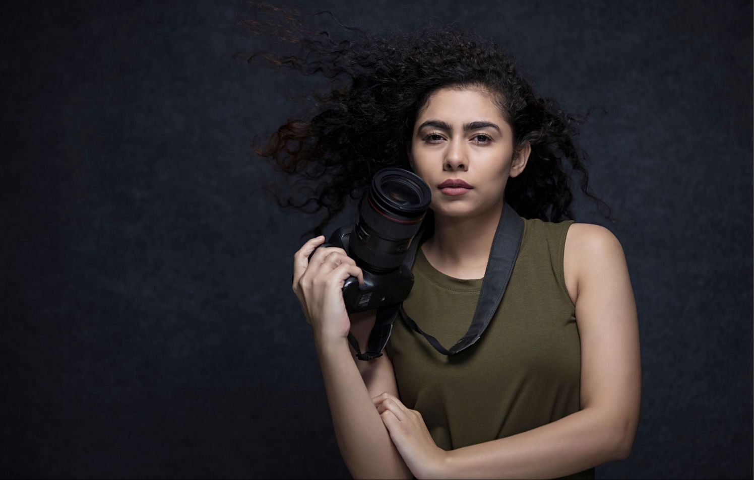 A person in an olive green tank top poses against a dark background in a dramatic portrait series.