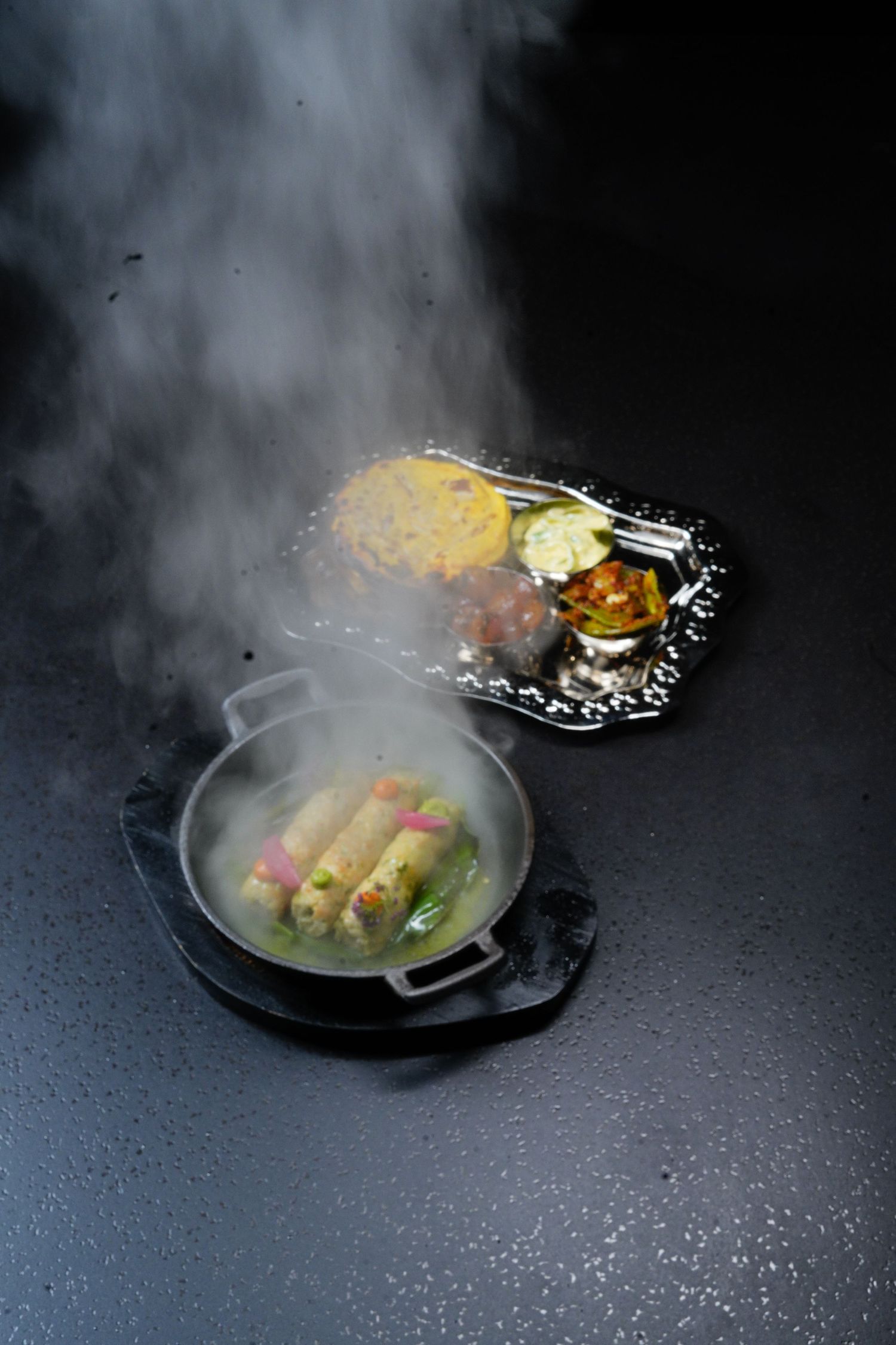 Steaming hot dish served on black plate with dramatic smoke effect creates an elegant fine dining presentation.