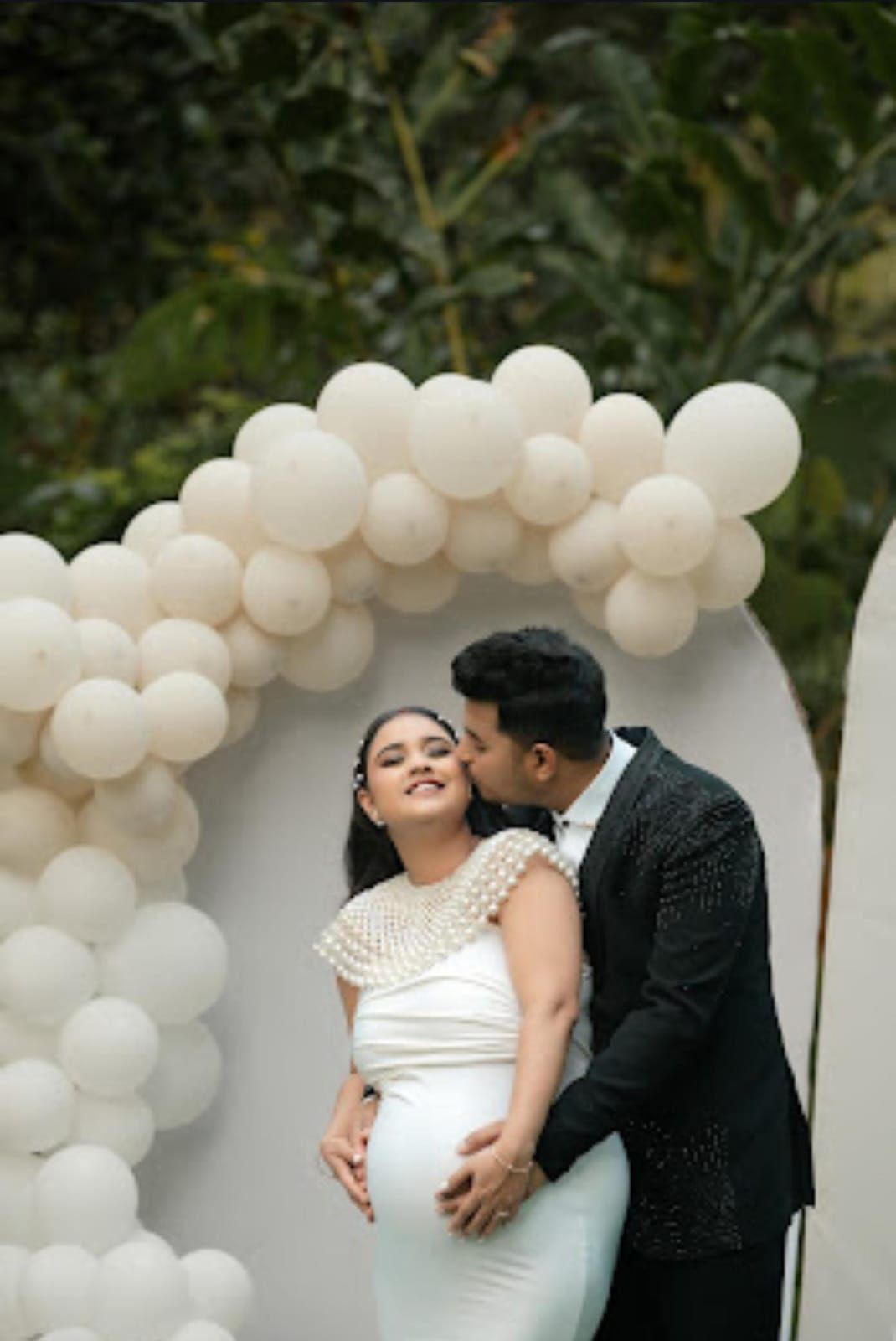Romantic couple moment under white balloon arch during celebration.