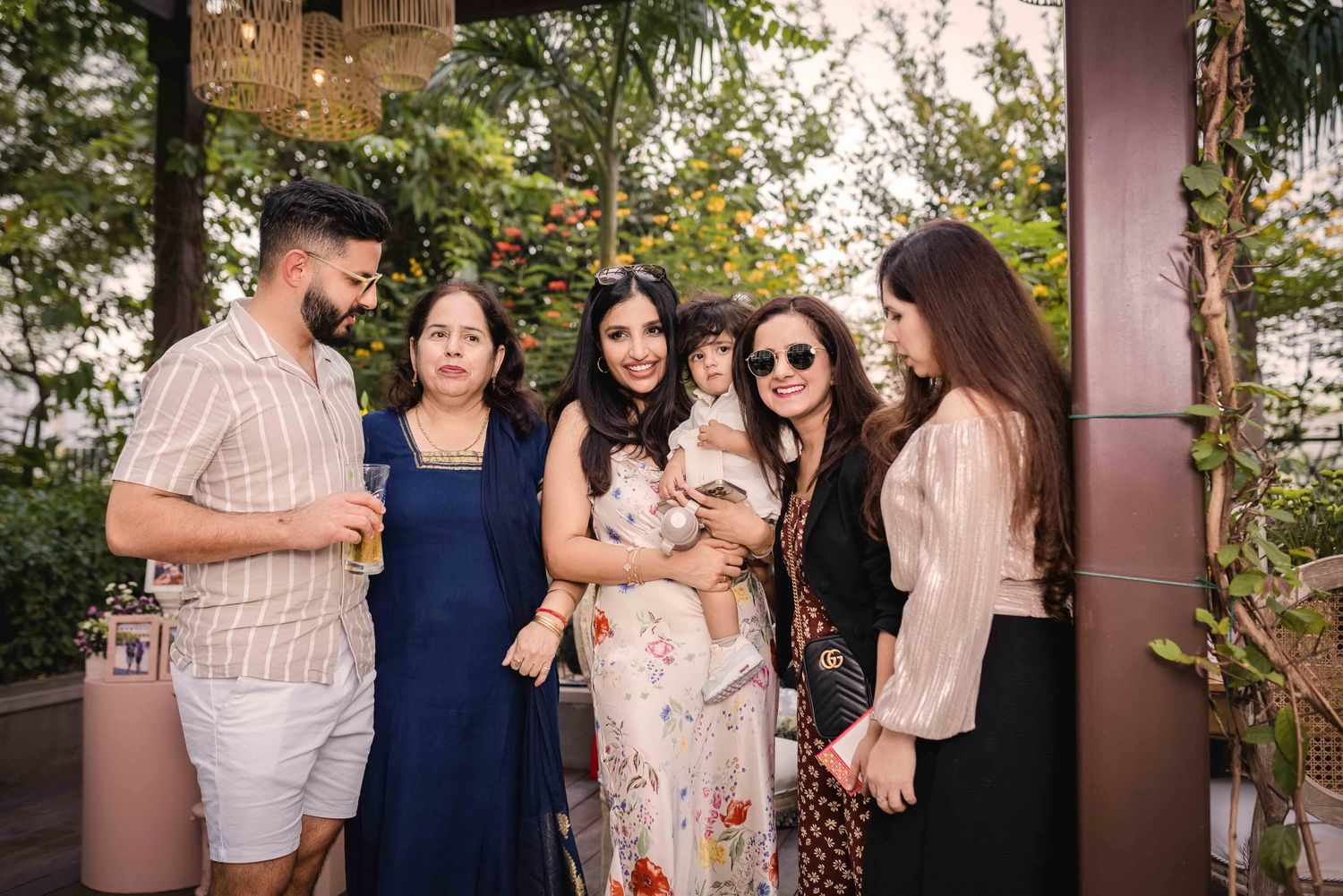 Family group of five adults and a baby gathered together at an outdoor garden celebration event.