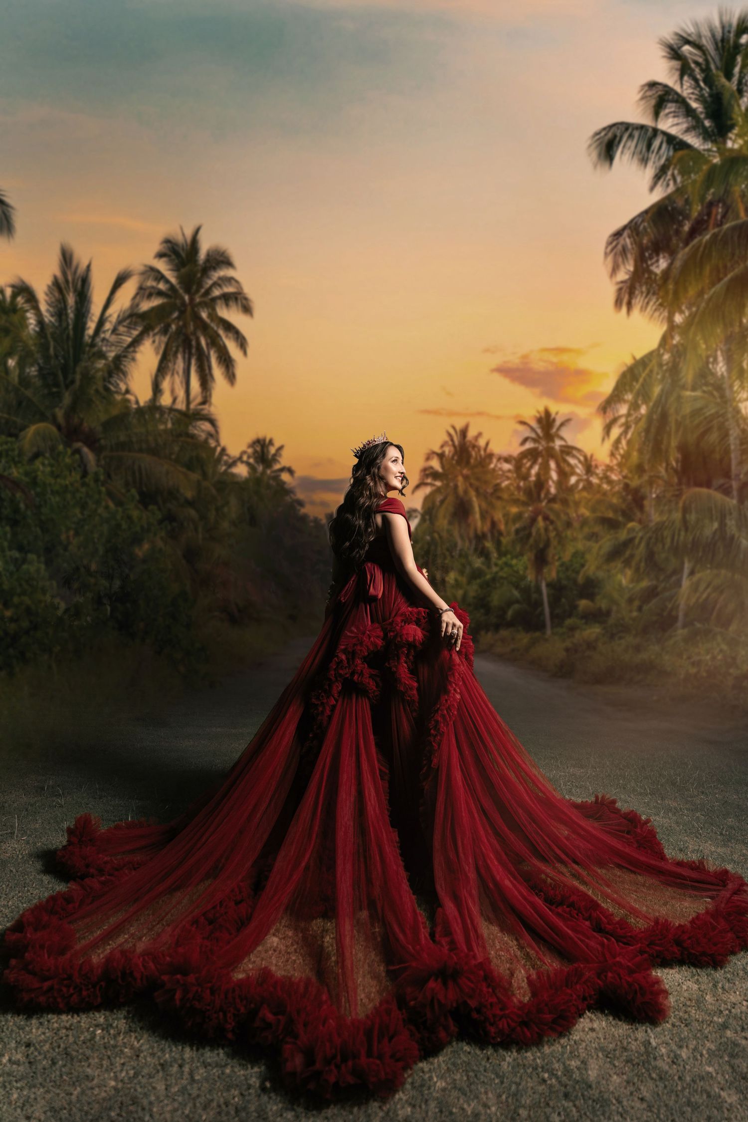 Woman in red ballgown with long train poses at sunset surrounded by tropical palm trees.