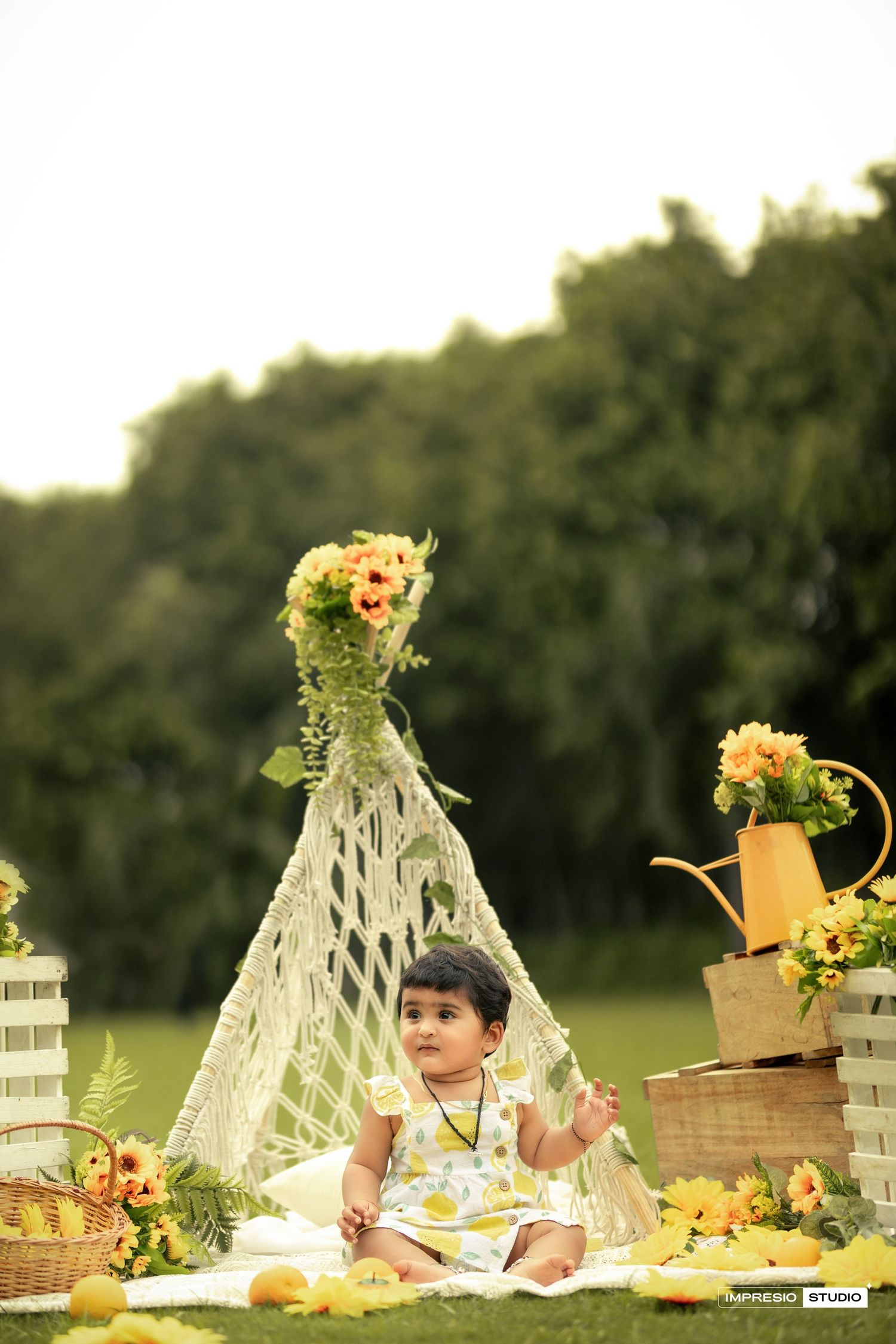 Outdoor picnic setup with lace teepees, floral arrangements and food spread on a grassy field at sunset.