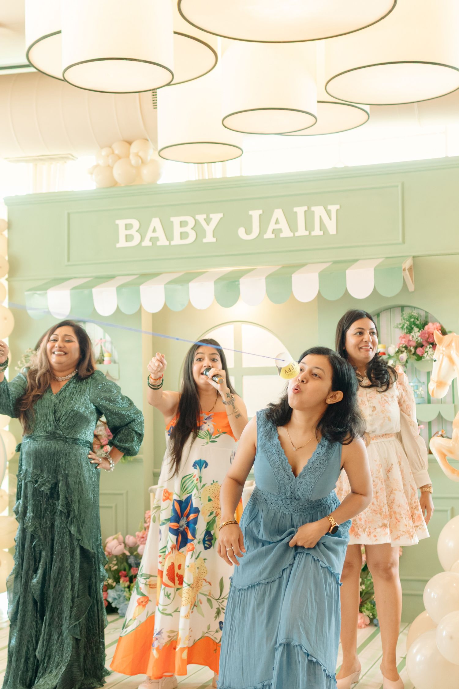 Four women celebrating at a Baby Jain shower party with balloons and floral decorations indoors.