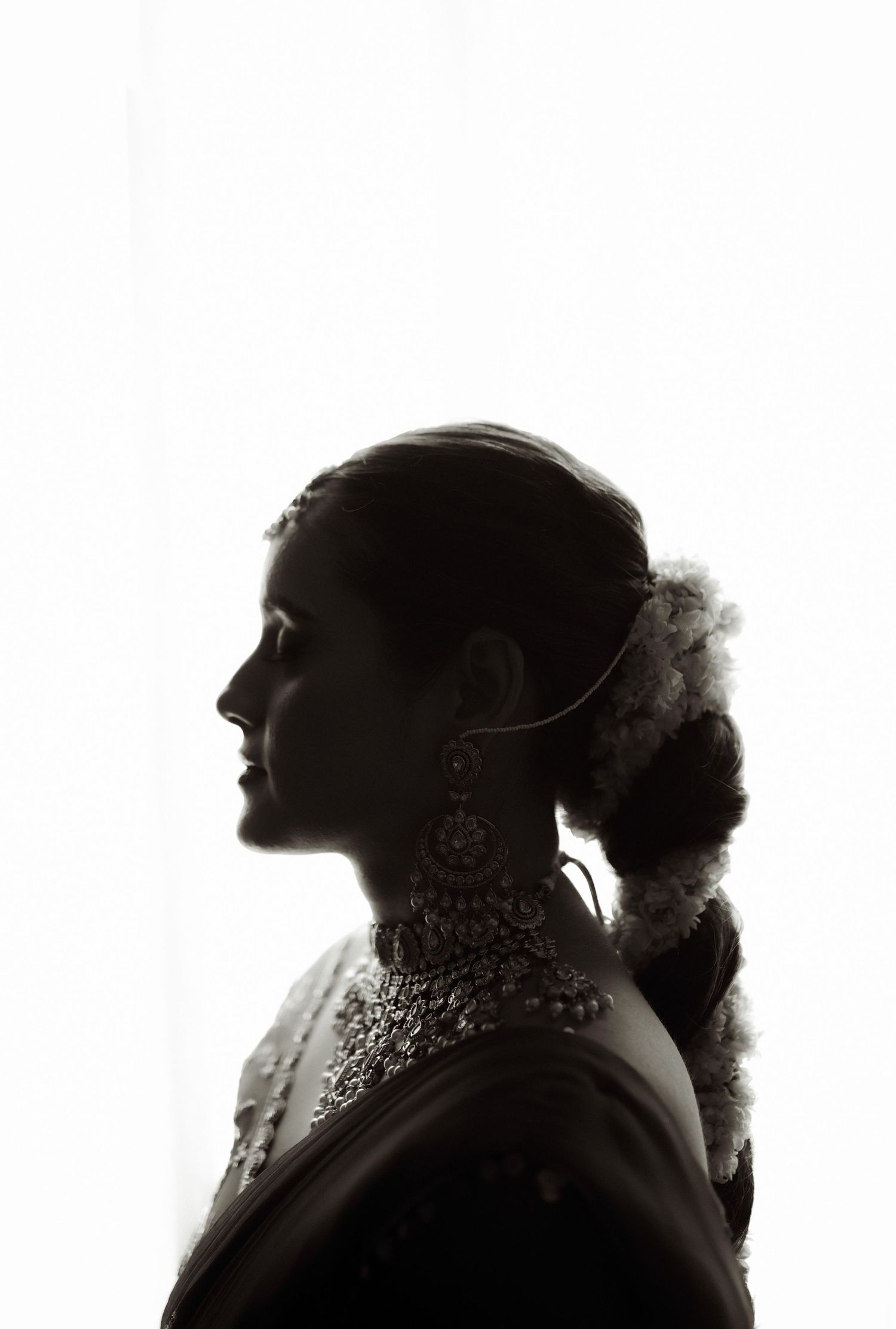 Silhouette of a woman in profile wearing ornate jewelry and traditional attire against a bright white background.