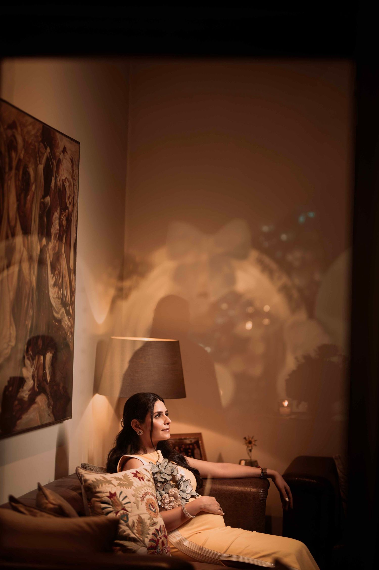 Woman relaxing on a couch in a warmly lit room with projected images on the wall behind her.