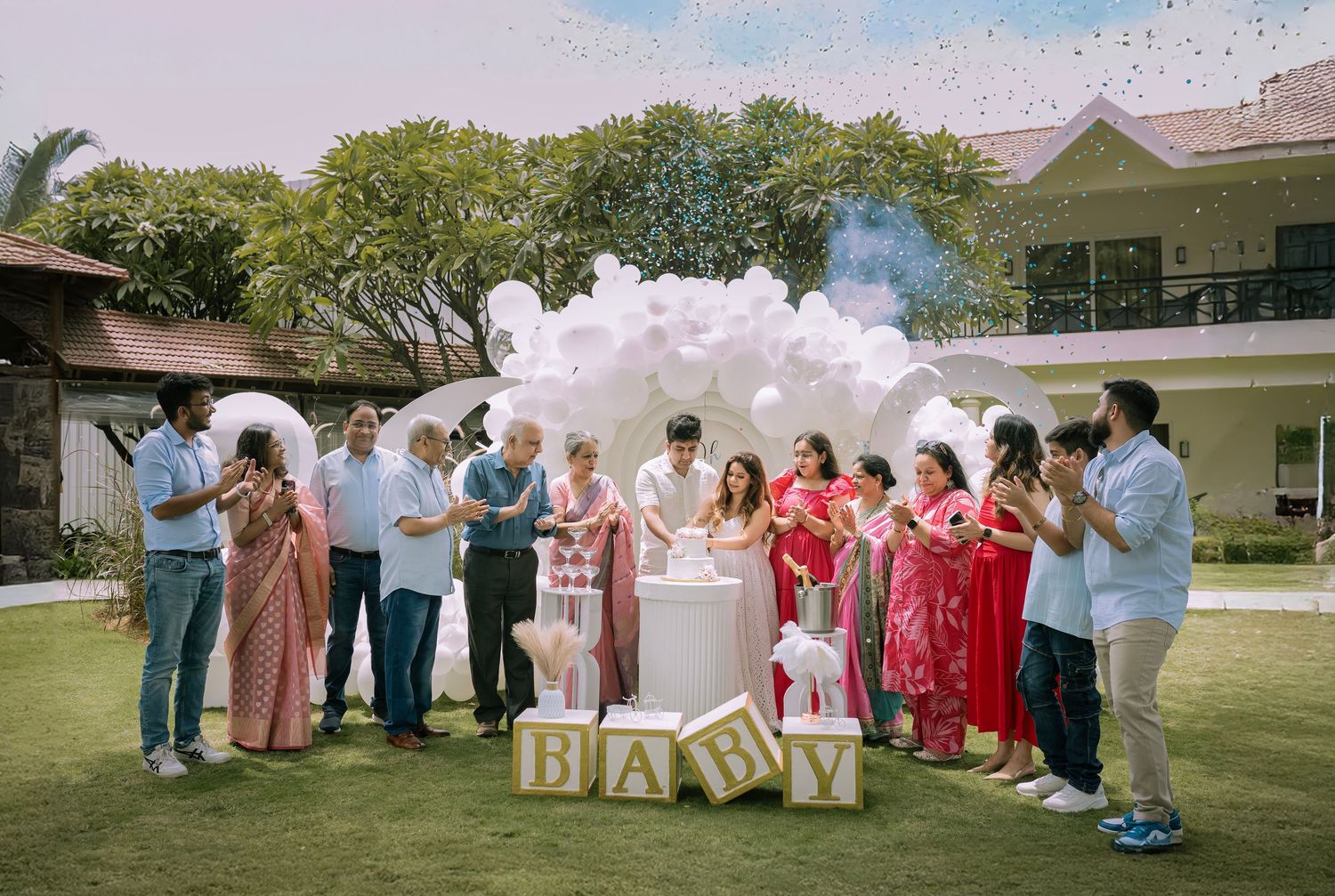 Family gathered outdoors for a baby gender reveal party with balloon arch and BABY blocks decoration.