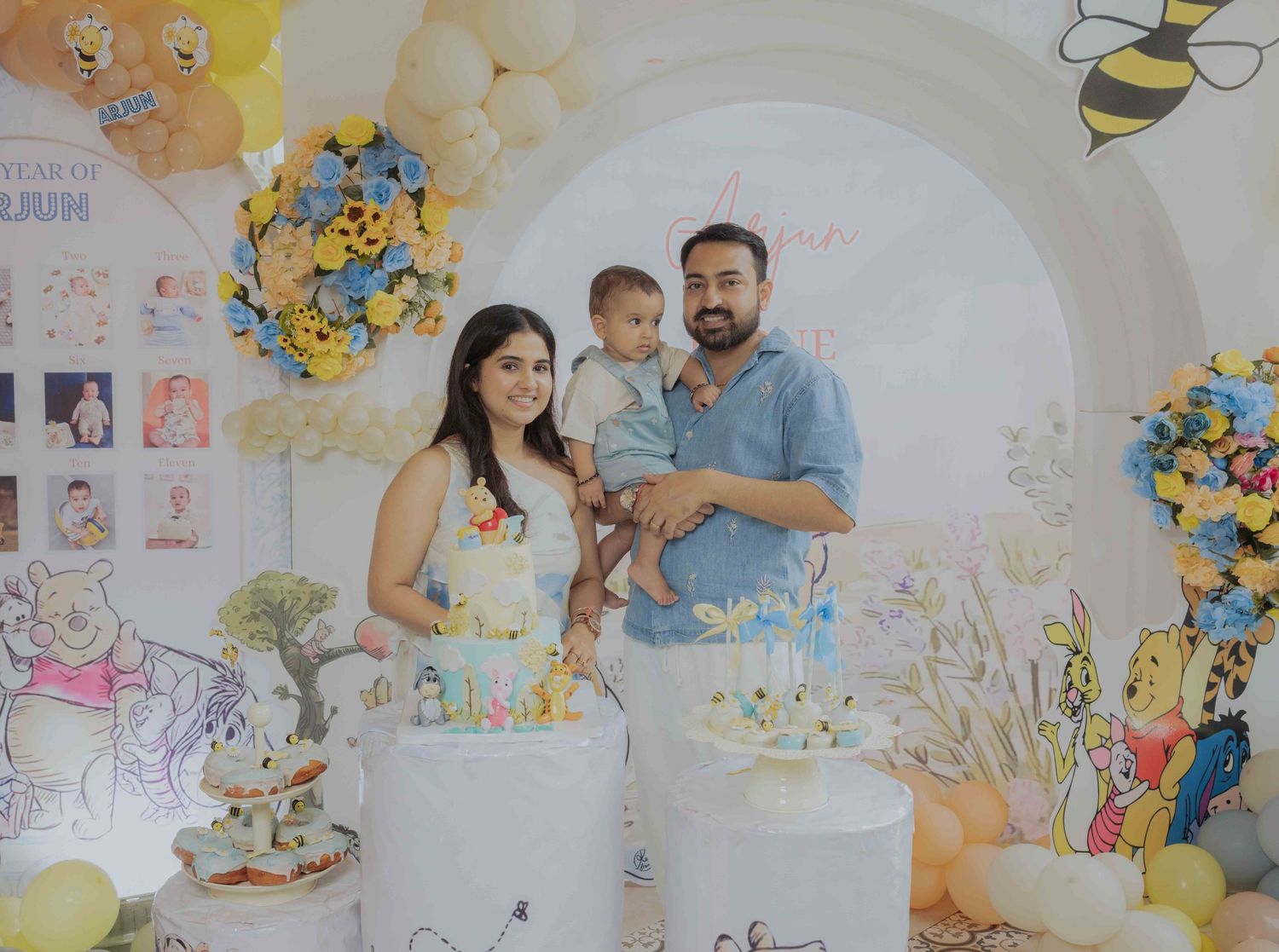 Family celebrating baby's first birthday with Winnie the Pooh themed decorations, cake, and balloons.