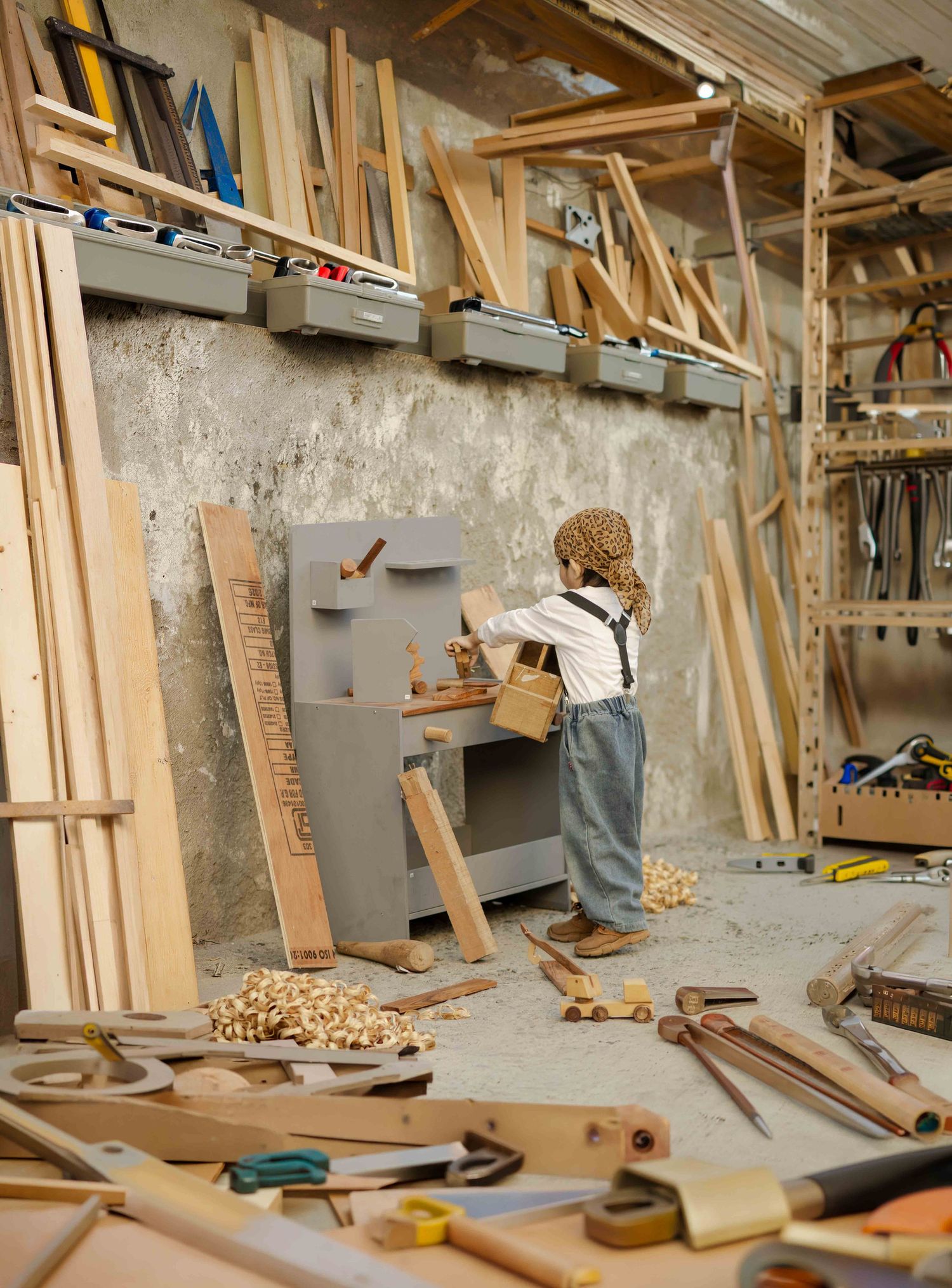 Child woodworker playing at a toy workbench in a rustic carpentry workshop surrounded by tools and lumber.