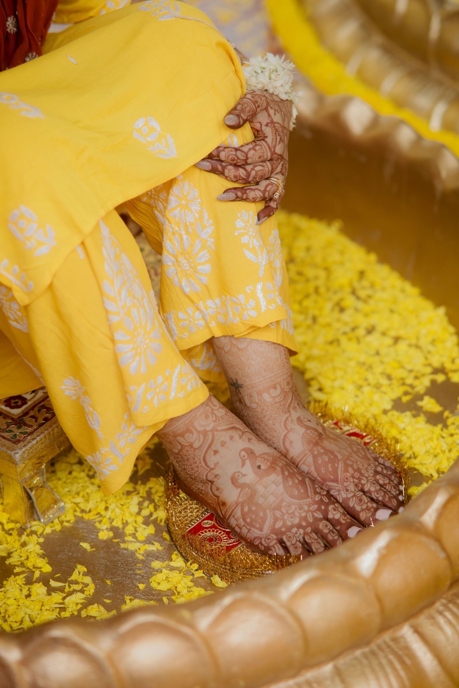 Intricate henna designs adorn feet surrounded by yellow flower petals in a traditional Indian wedding ritual.