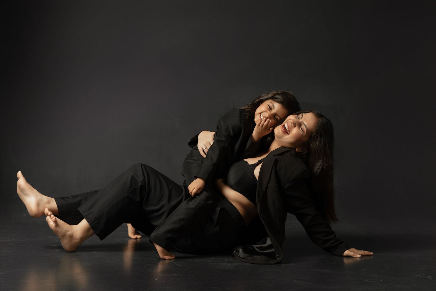 Two barefoot dancers in black clothing pose dramatically on a dark studio floor in an expressive contemporary dance performance.
