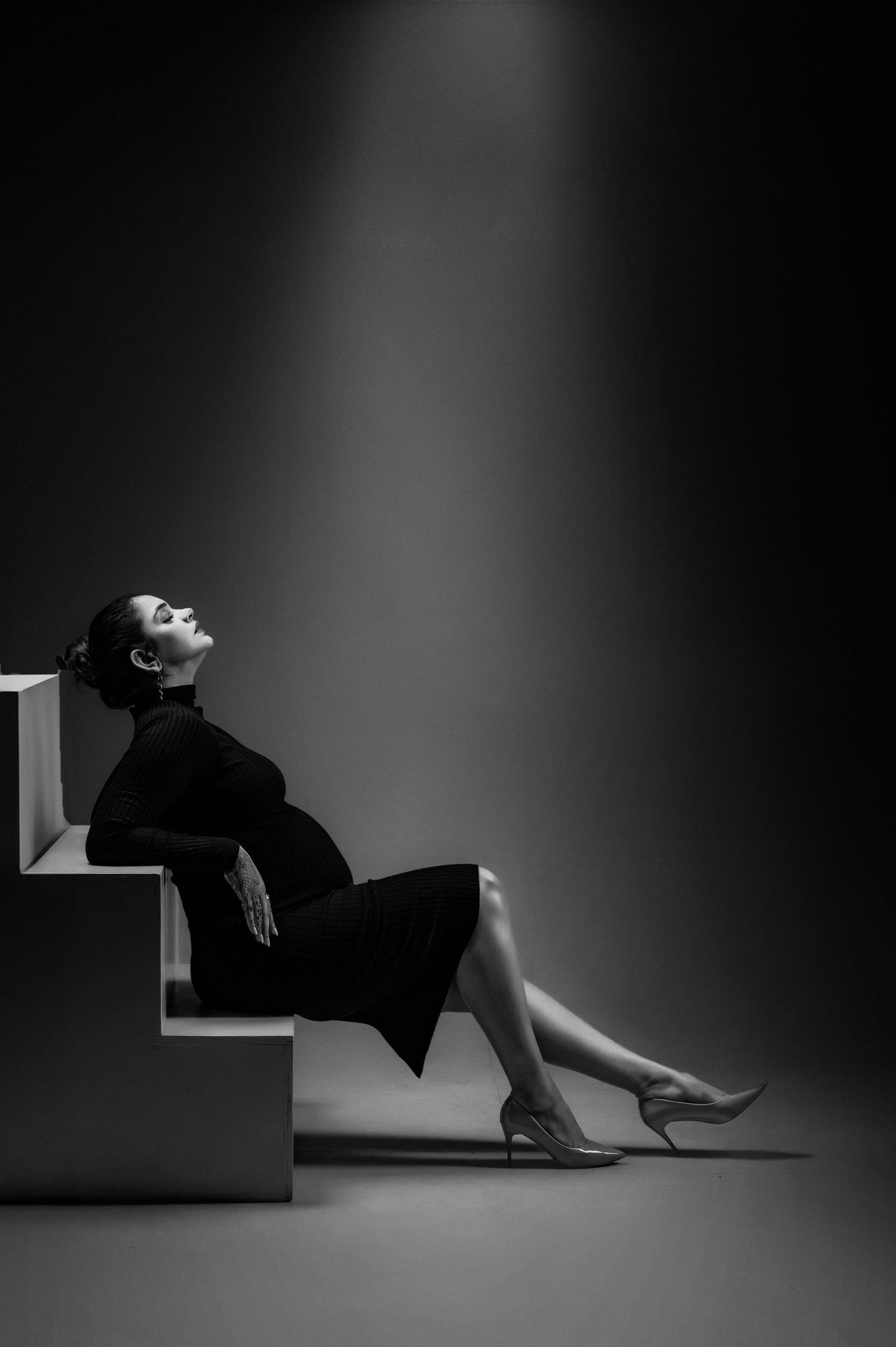 Film noir style photography with model posed dramatically on angular white platform.
