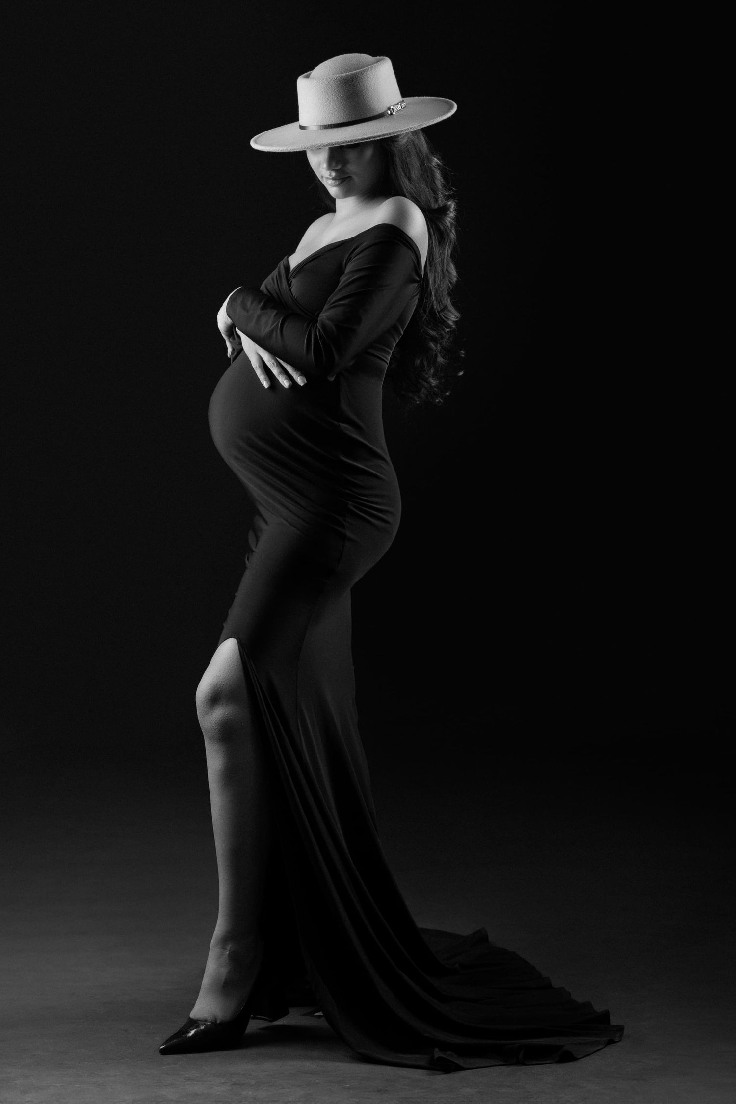 Dramatic maternity poses with hat in dark studio setting.
