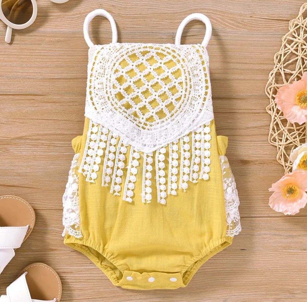 Yellow and white crochet baby outfit with decorative fringe detail displayed with flowers.