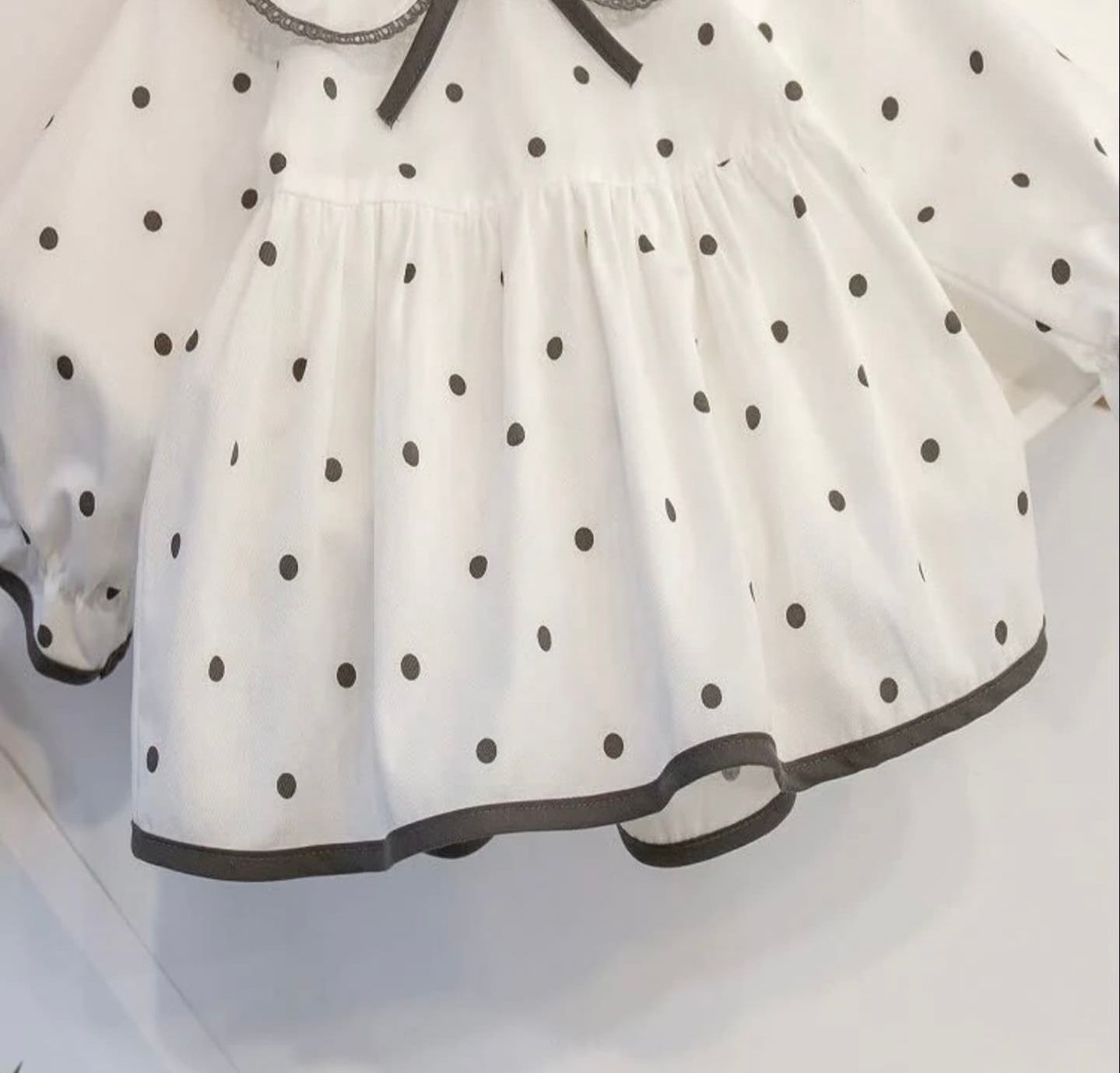 White polka dot dress fabric with gray trim detail along the hemline.
