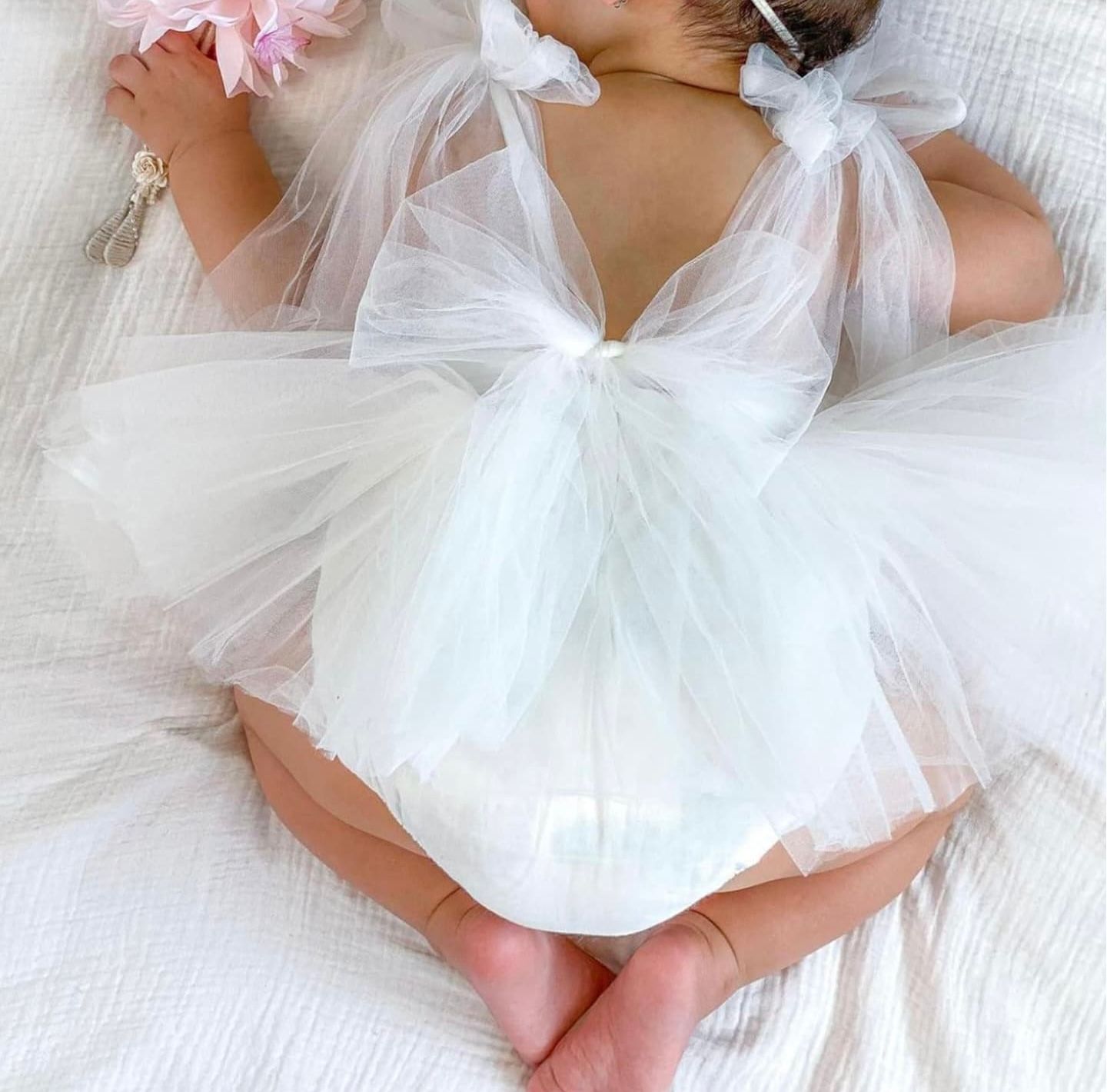 Newborn baby's feet wrapped in delicate white tulle fabric against a soft white background.