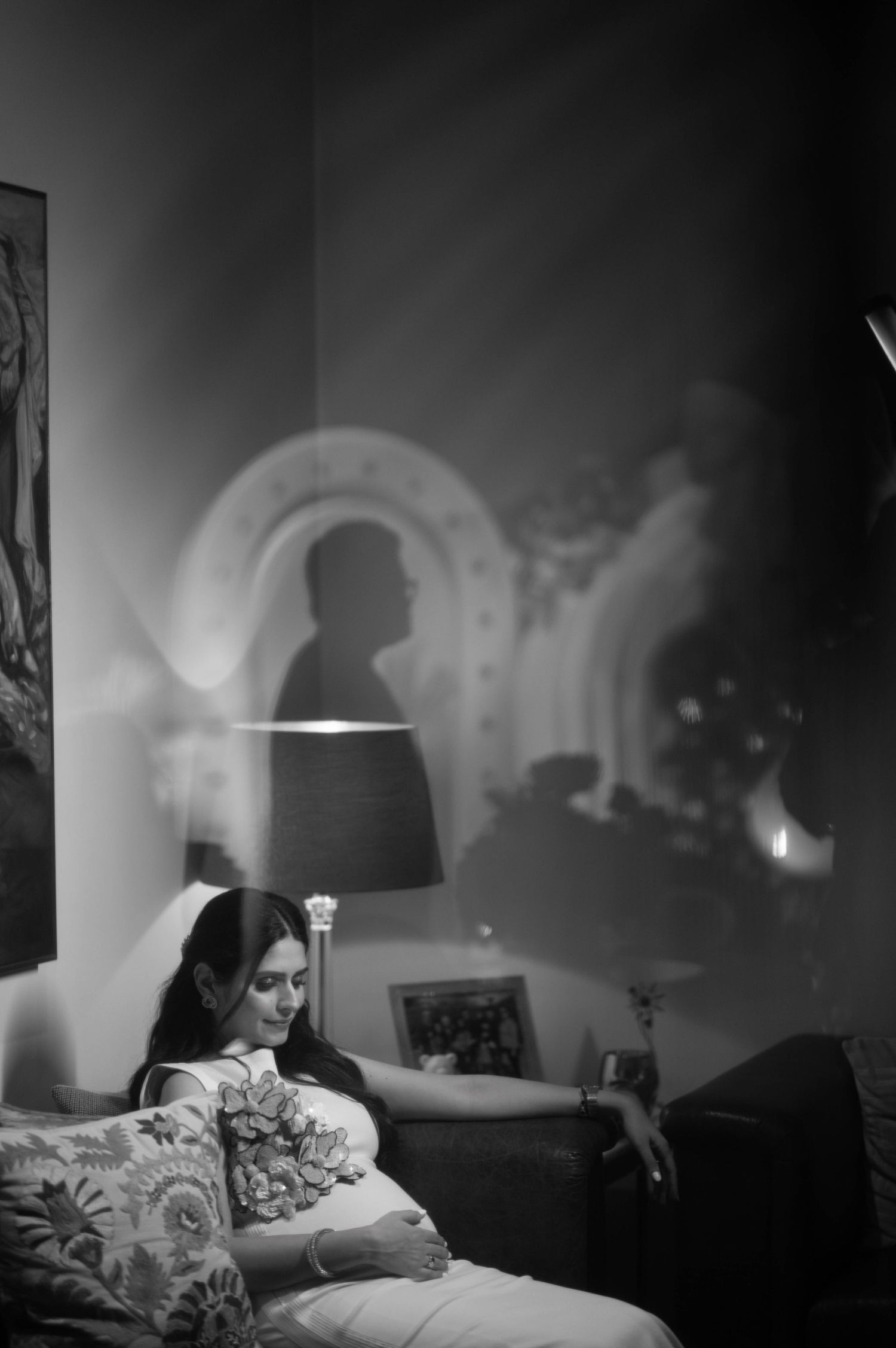 Black and white photo of a woman resting on a sofa with a dramatic shadow projection on the wall behind her.