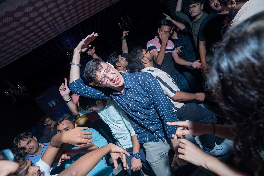 People dancing energetically at a crowded nightclub party, with a man in a striped shirt at the center.