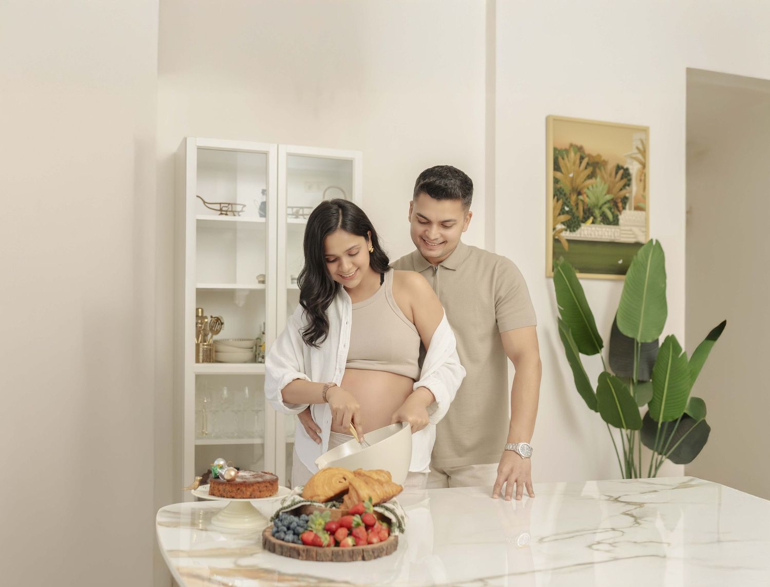 Pregnant couple preparing fresh fruit and croissants together in a bright, modern kitchen.