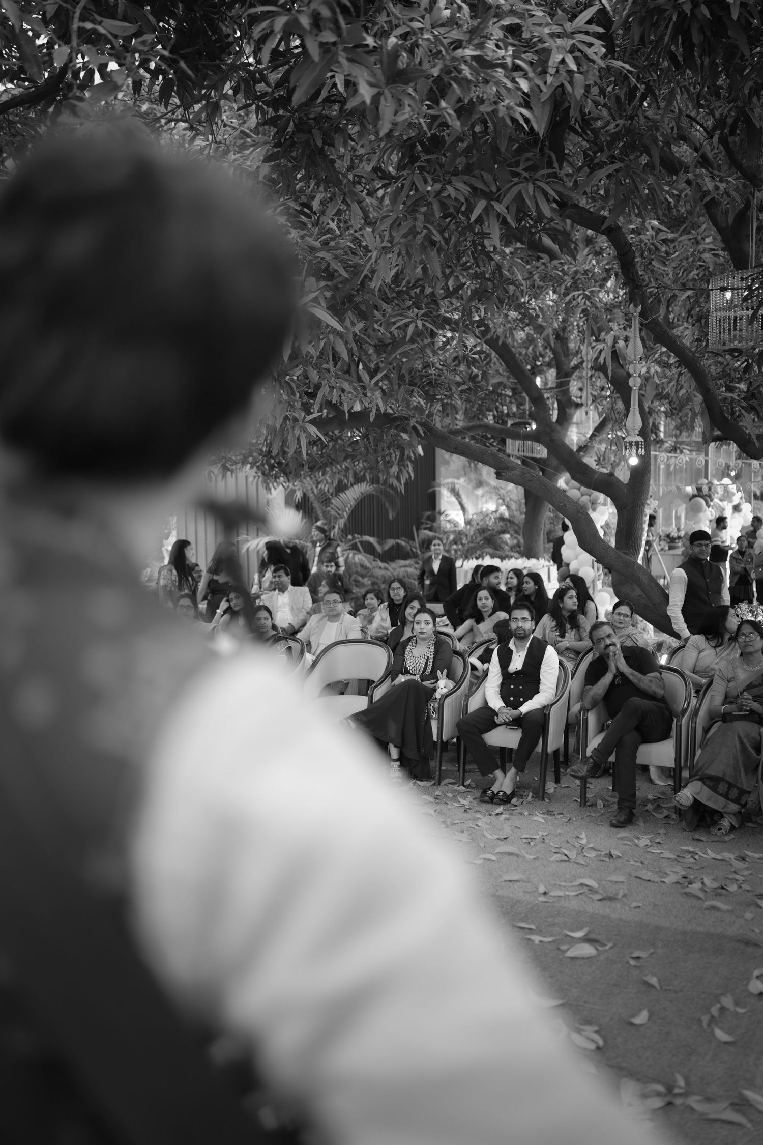 Black and white photo of an outdoor gathering with seated audience under trees at an evening event.