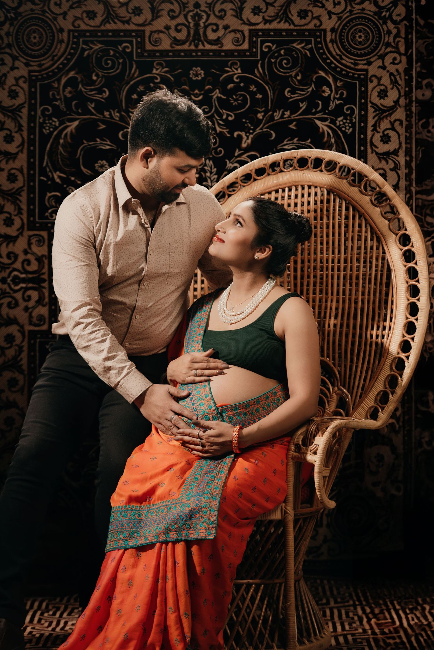 Intimate maternity portraits featuring a couple on a wicker chair with ornate backdrop.