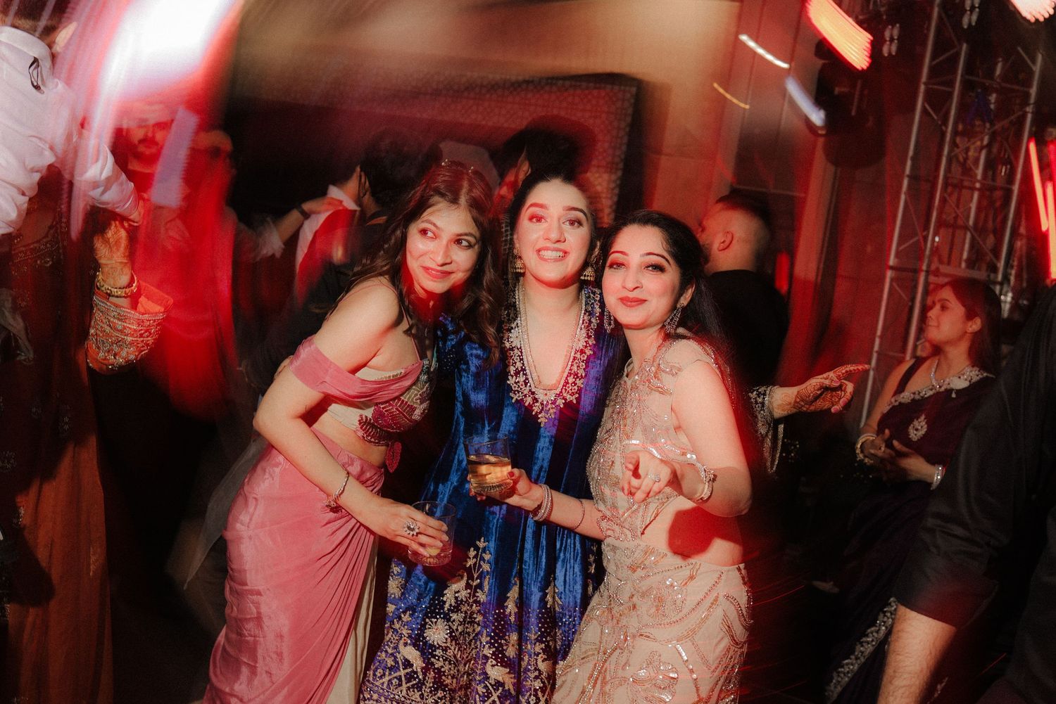 A group of people dancing and celebrating at a nightclub with red ambient lighting.