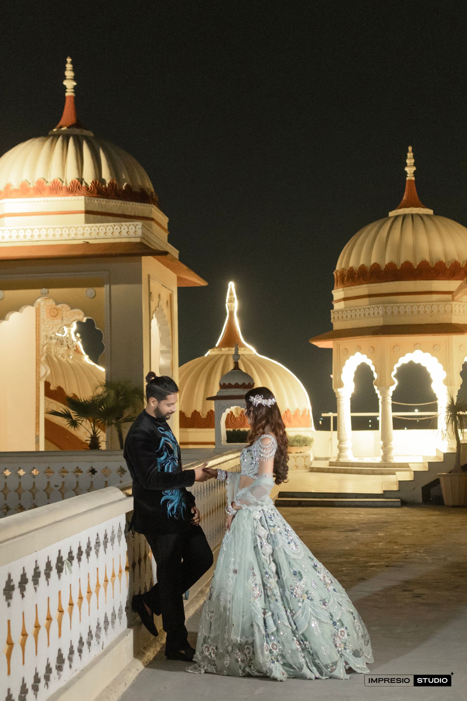 Couple in elegant attire sharing a romantic moment on a rooftop with illuminated Mughal domes at night.