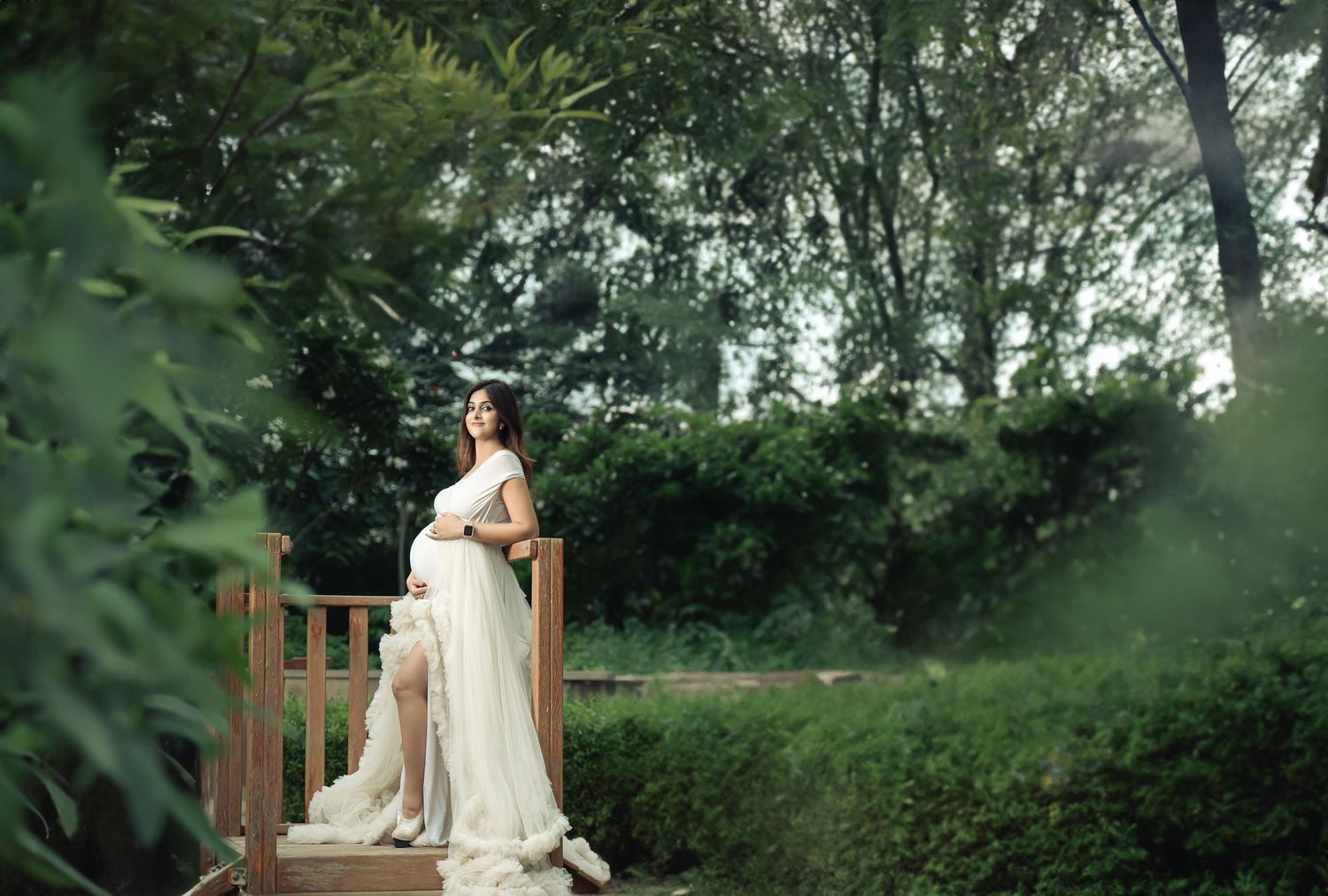 Artistic maternity photography in a lush green outdoor garden setting.