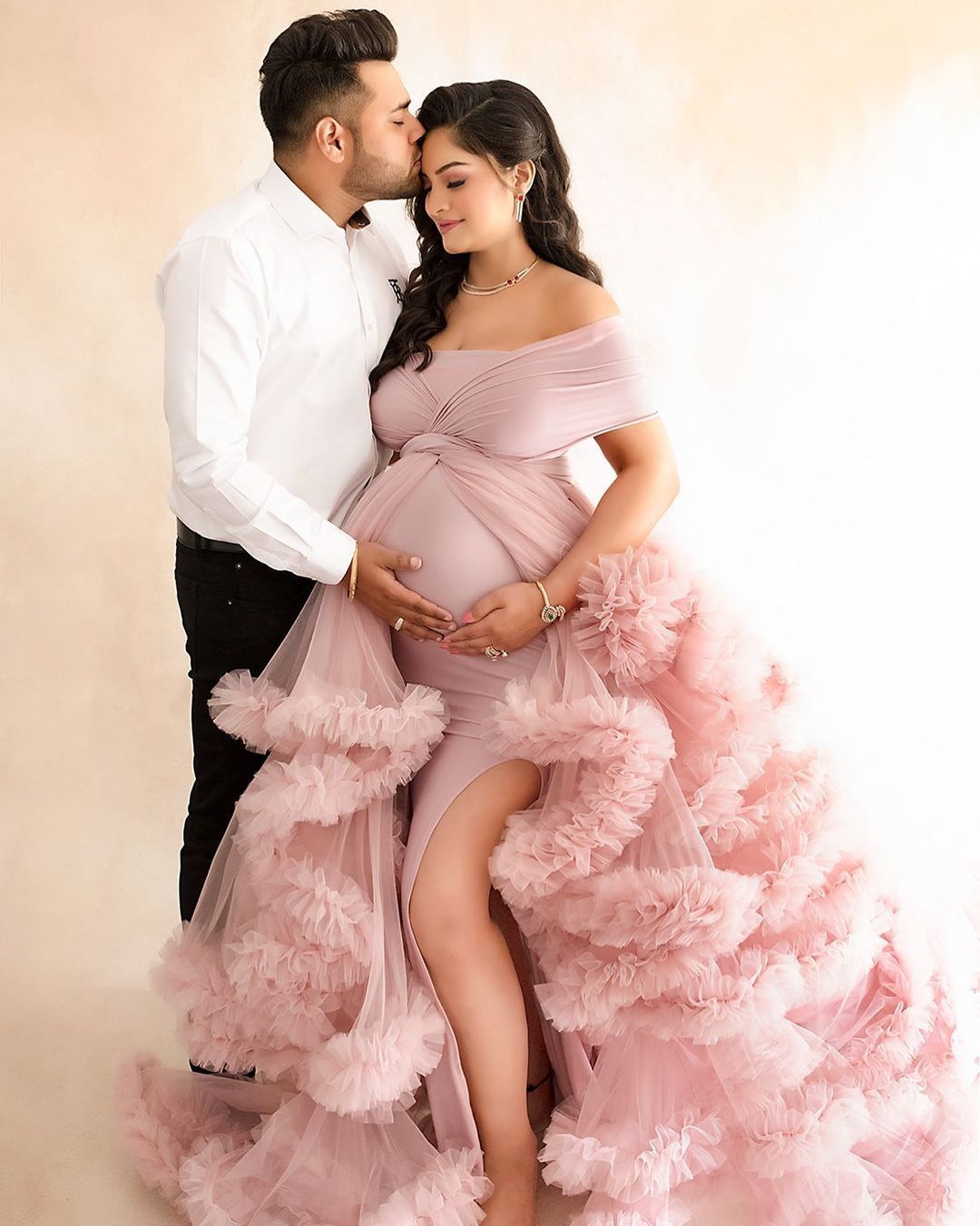 A romantic studio maternity portrait with a couple in pink tulle gown.