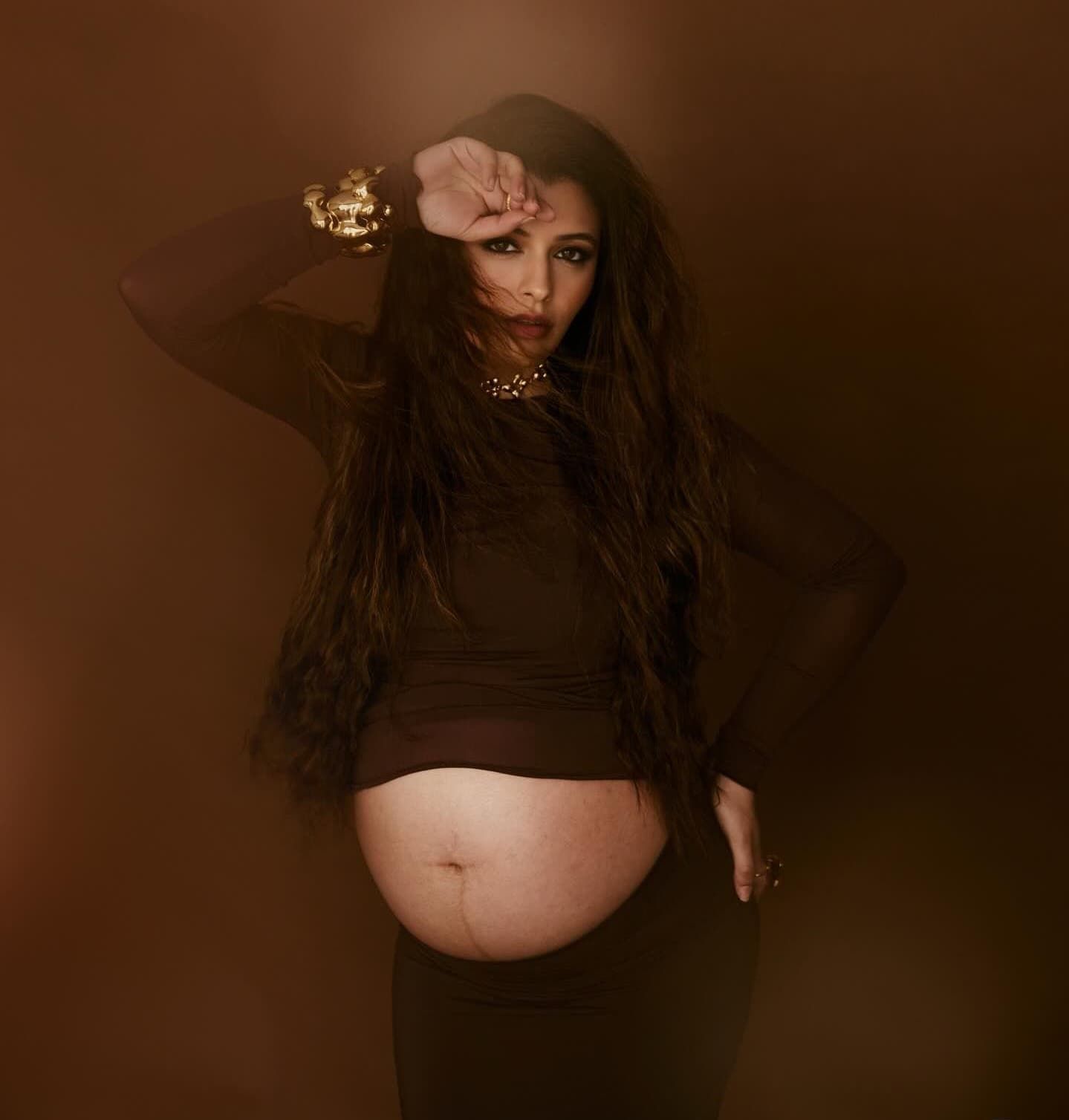 Dramatic maternity photoshoot with dark backdrop featuring elegant poses and flowing fabric.