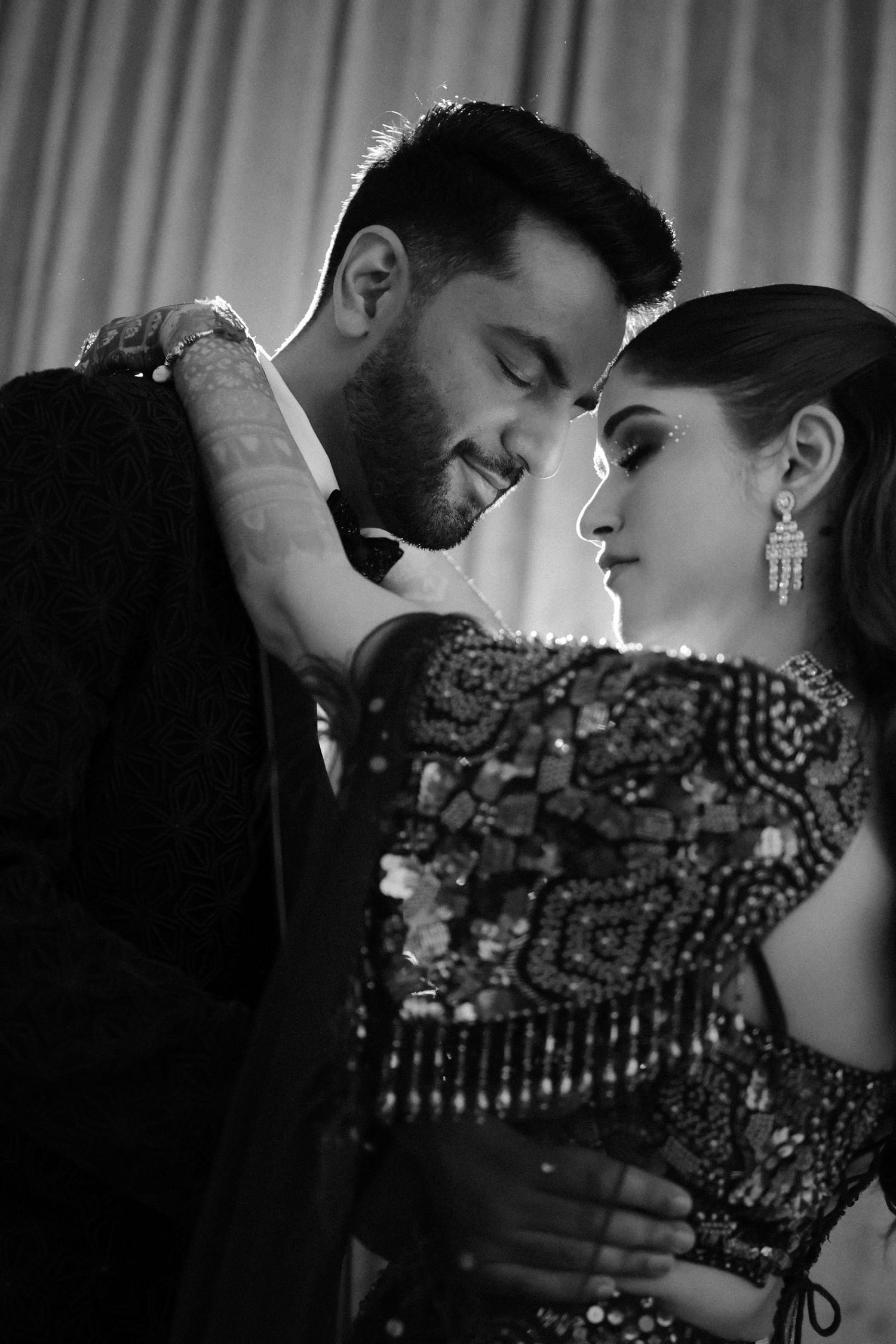 Black and white photo of an elegant couple in embroidered attire sharing an intimate moment at a formal event.