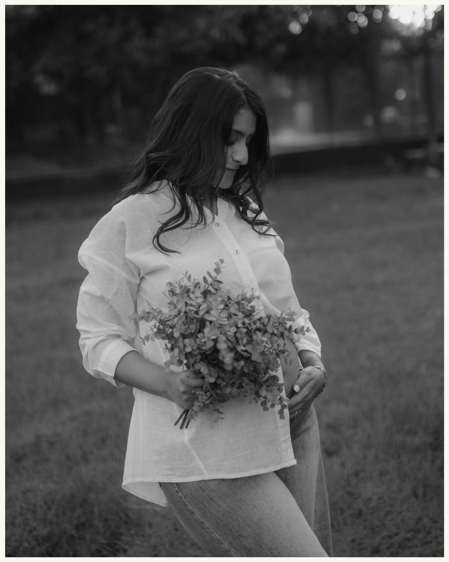 Black and white photo of a woman in a white blouse holding a bouquet of wildflowers outdoors.