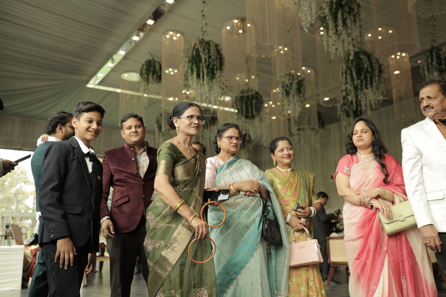 Group of elegantly dressed guests posing together at an Indian wedding celebration in a decorated venue.
