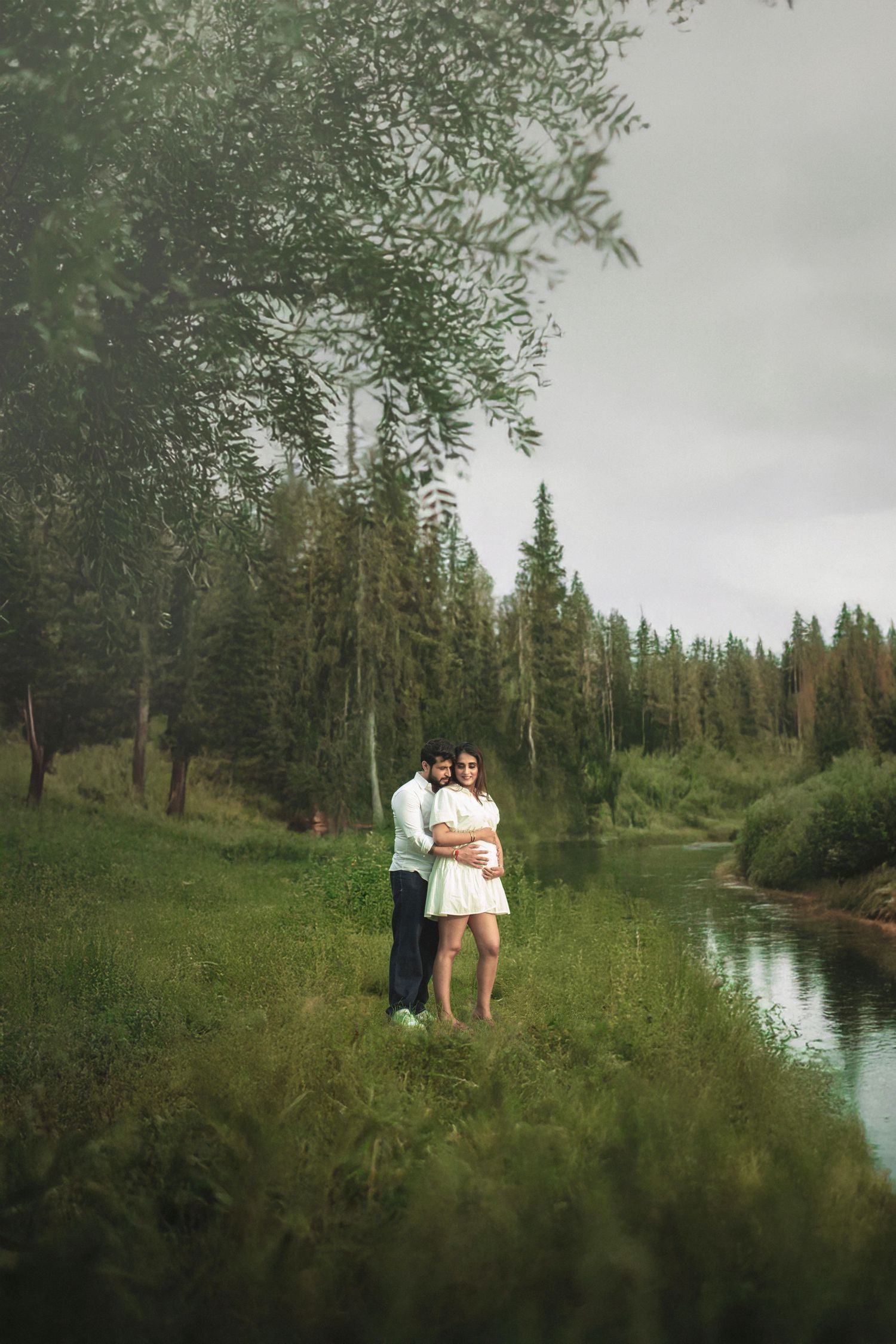 Scenic lakeside maternity photo session with evergreen trees and calm water in the background.