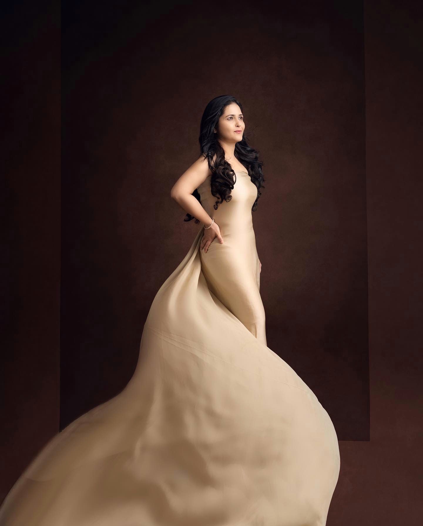 Dramatic maternity portrait with flowing cream colored dress in moody lighting.