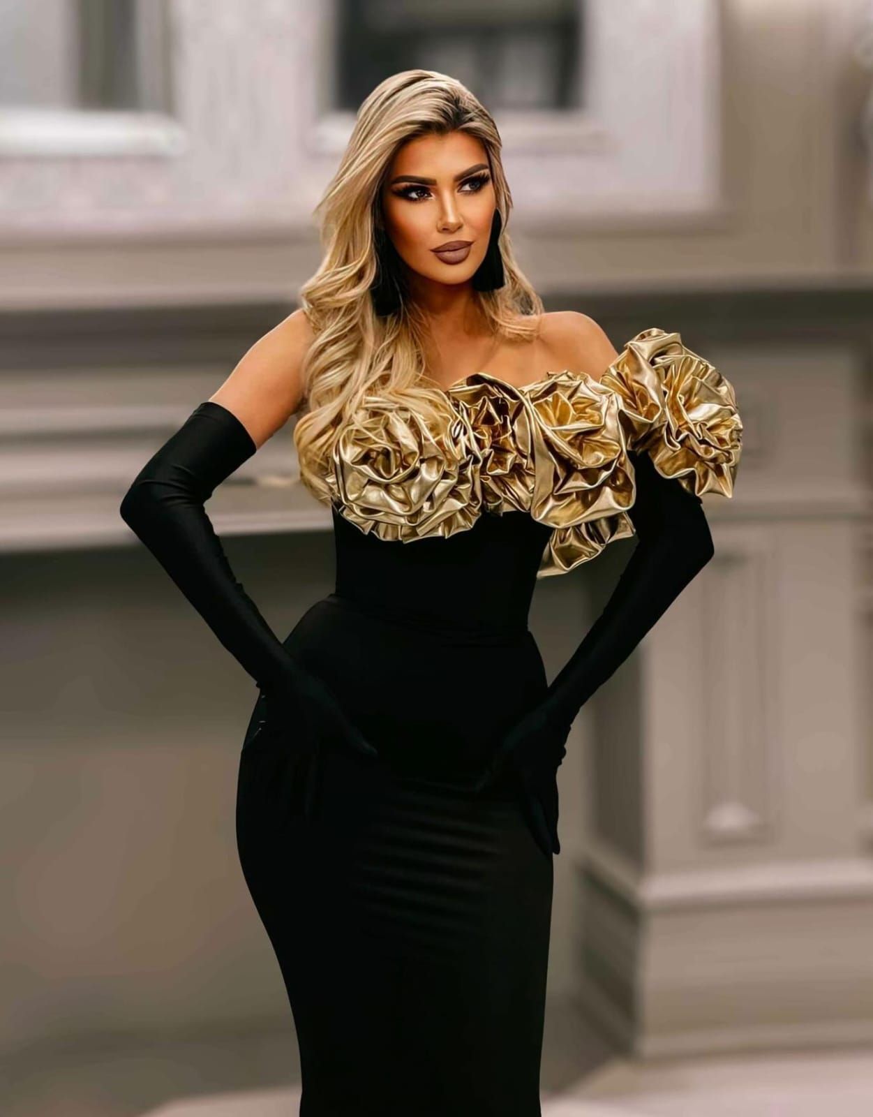 Fashion photoshoot featuring black gown with metallic gold shoulder detail against neutral backdrop.