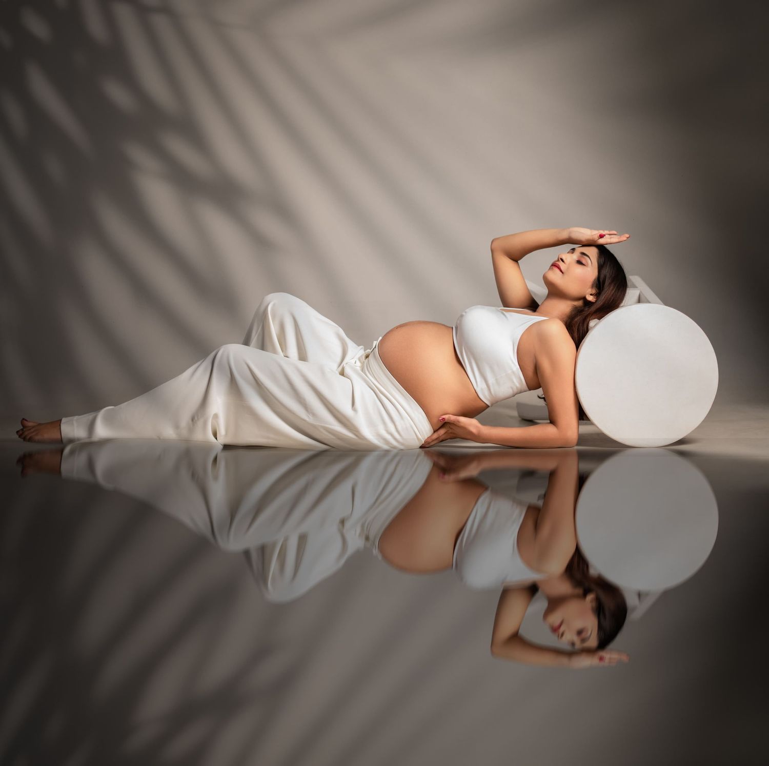Artistic maternity photo with reflection and dramatic shadows on glossy floor.