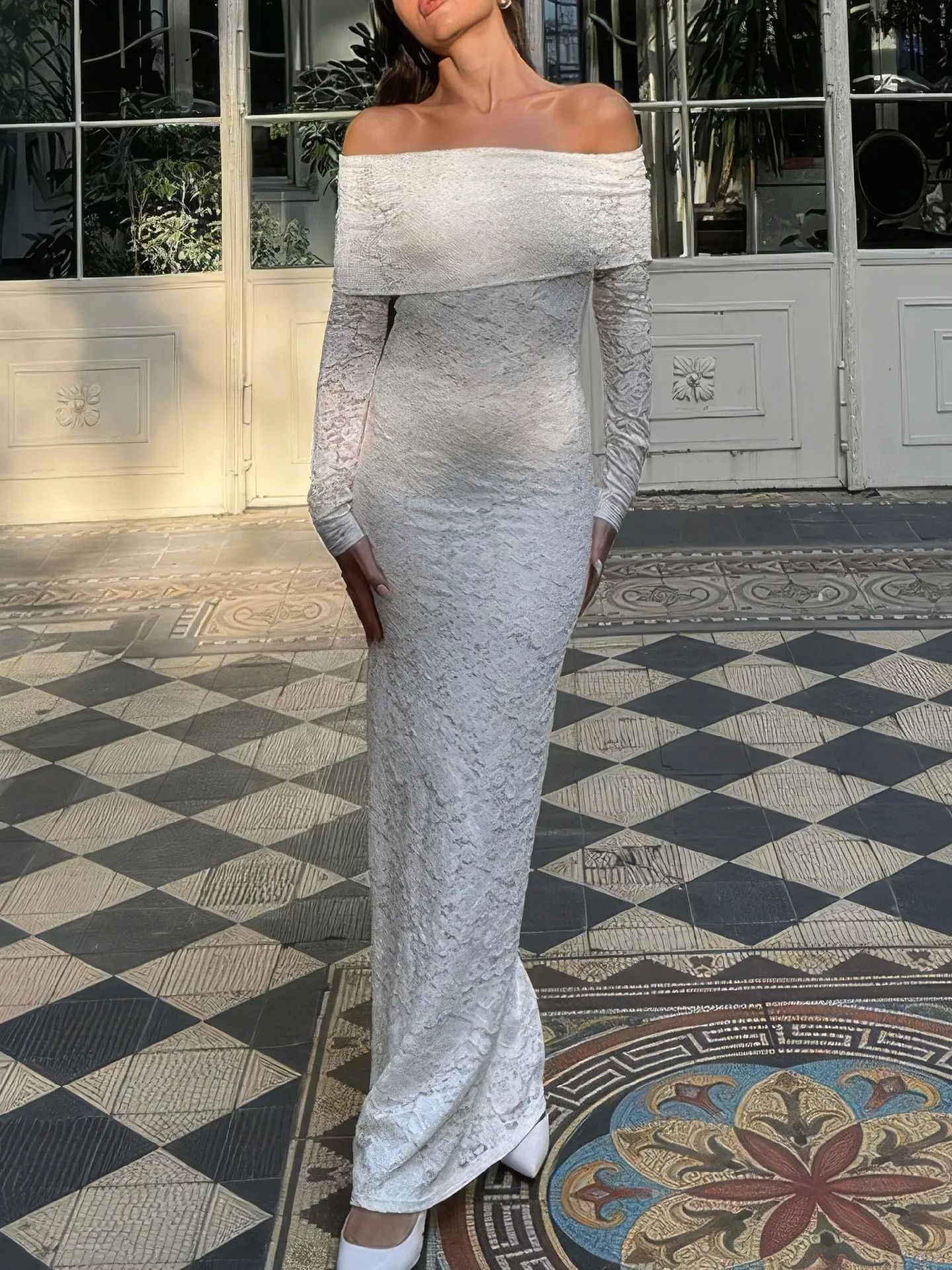 Woman in fitted white lace dress poses on ornate tiled floor with architectural details.