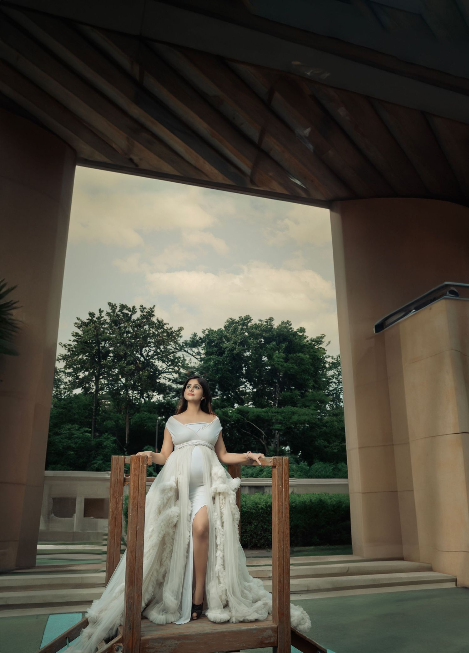Elegant maternity photos under a covered outdoor walkway with architectural elements.