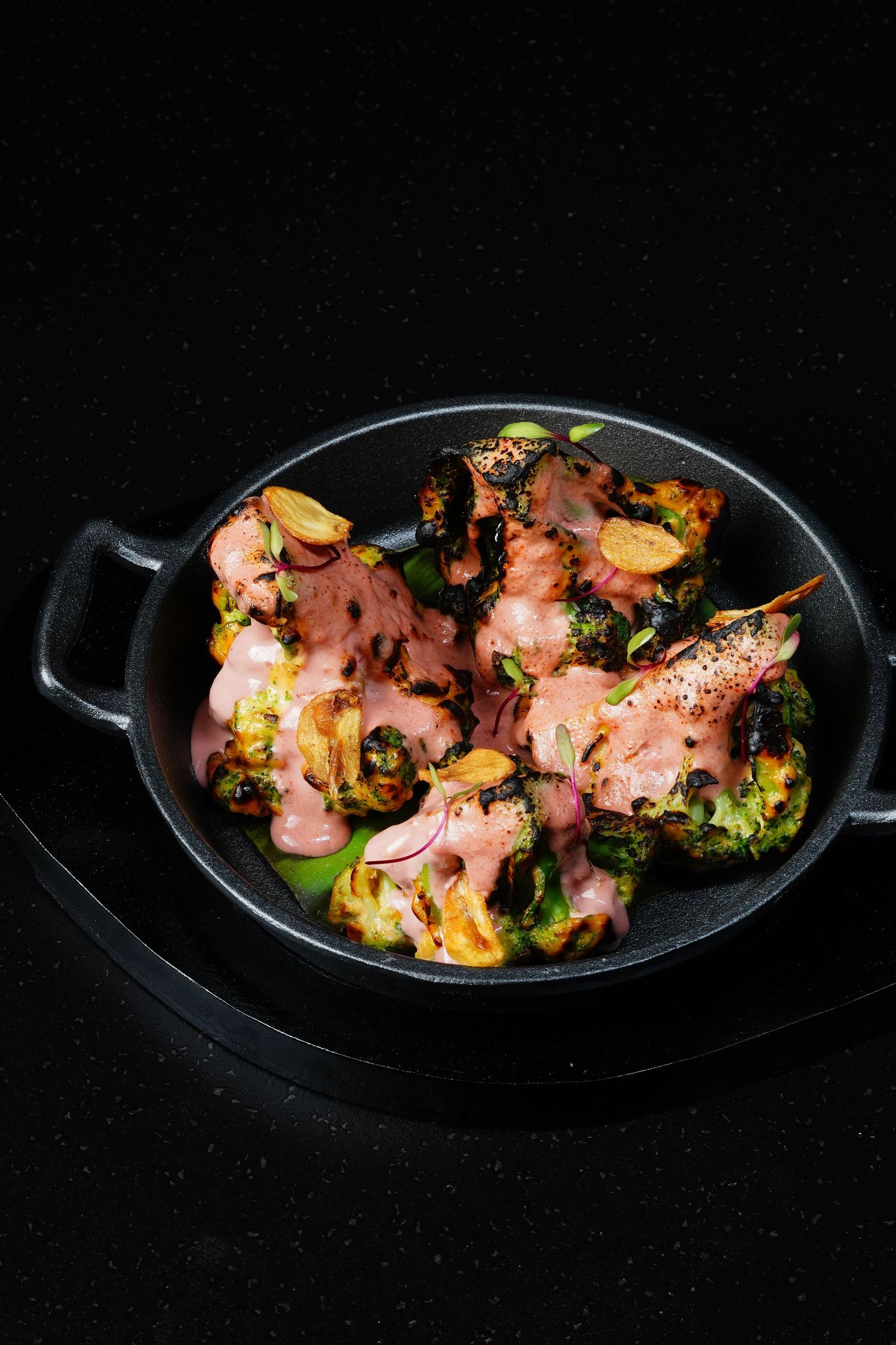 Grilled chicken with roasted brussels sprouts and vegetables served in a black cast iron pan on dark background.