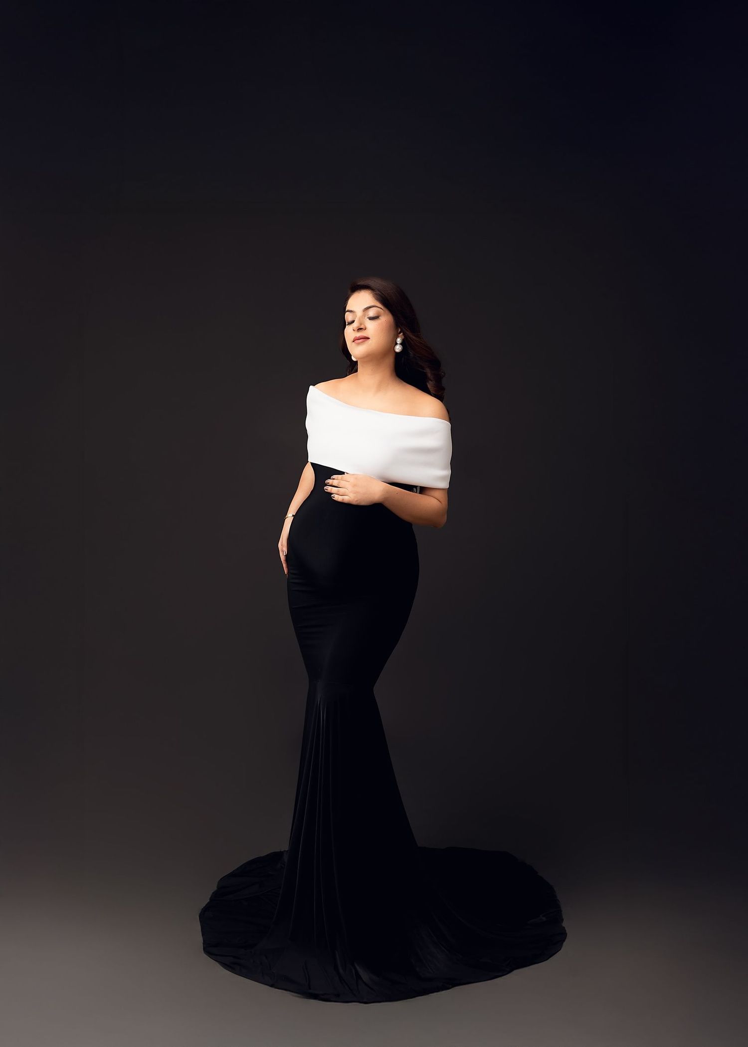 Elegant off-shoulder black mermaid gown against dark background in dramatic studio portrait.